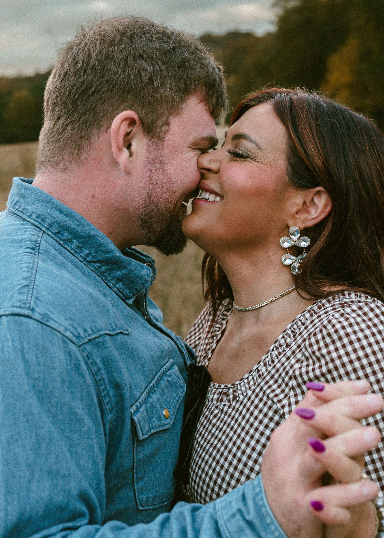 Romantic couple in denim and gingham sharing intimate moments outdoors.