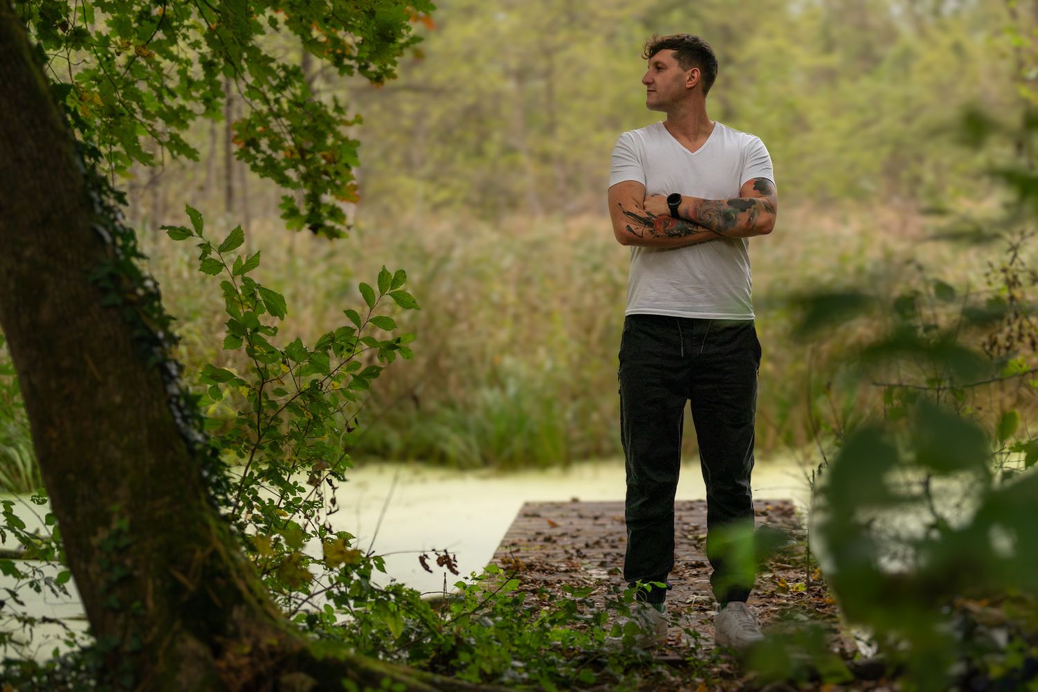 Person in white t-shirt standing in natural outdoor setting with trees.
