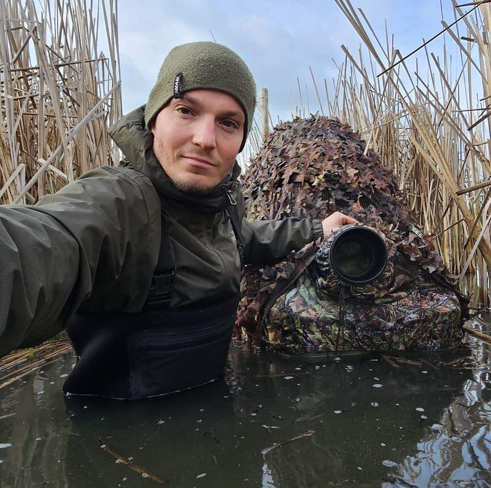 Wildlife photographer camouflaged in reeds while taking photos in wetland environment.