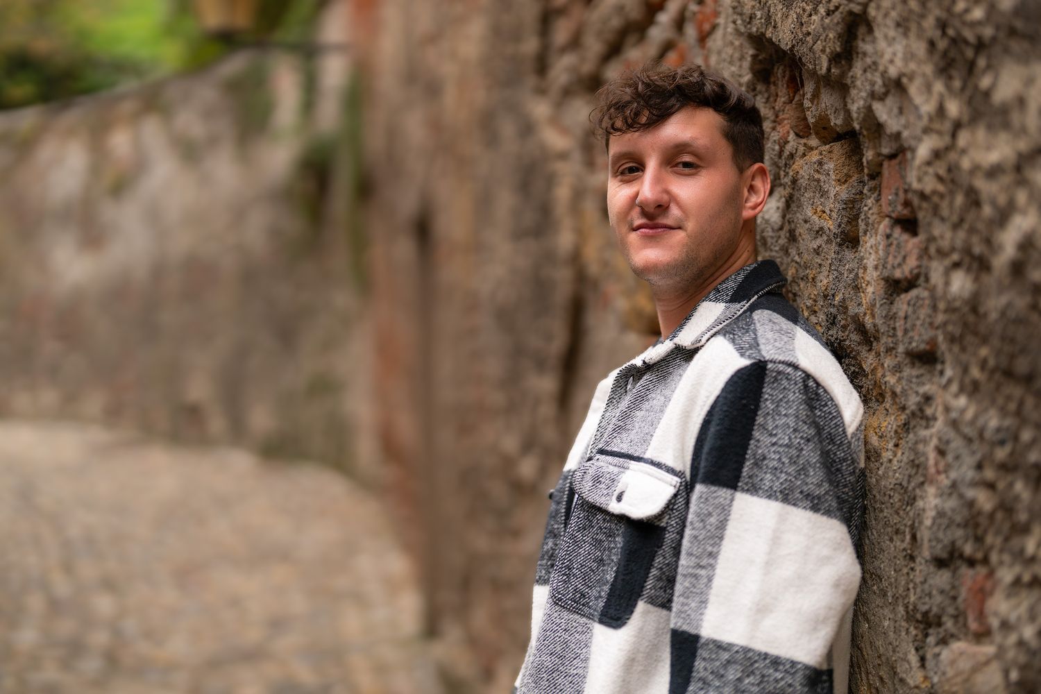 Person wearing plaid jacket poses against textured tree bark in outdoor setting.