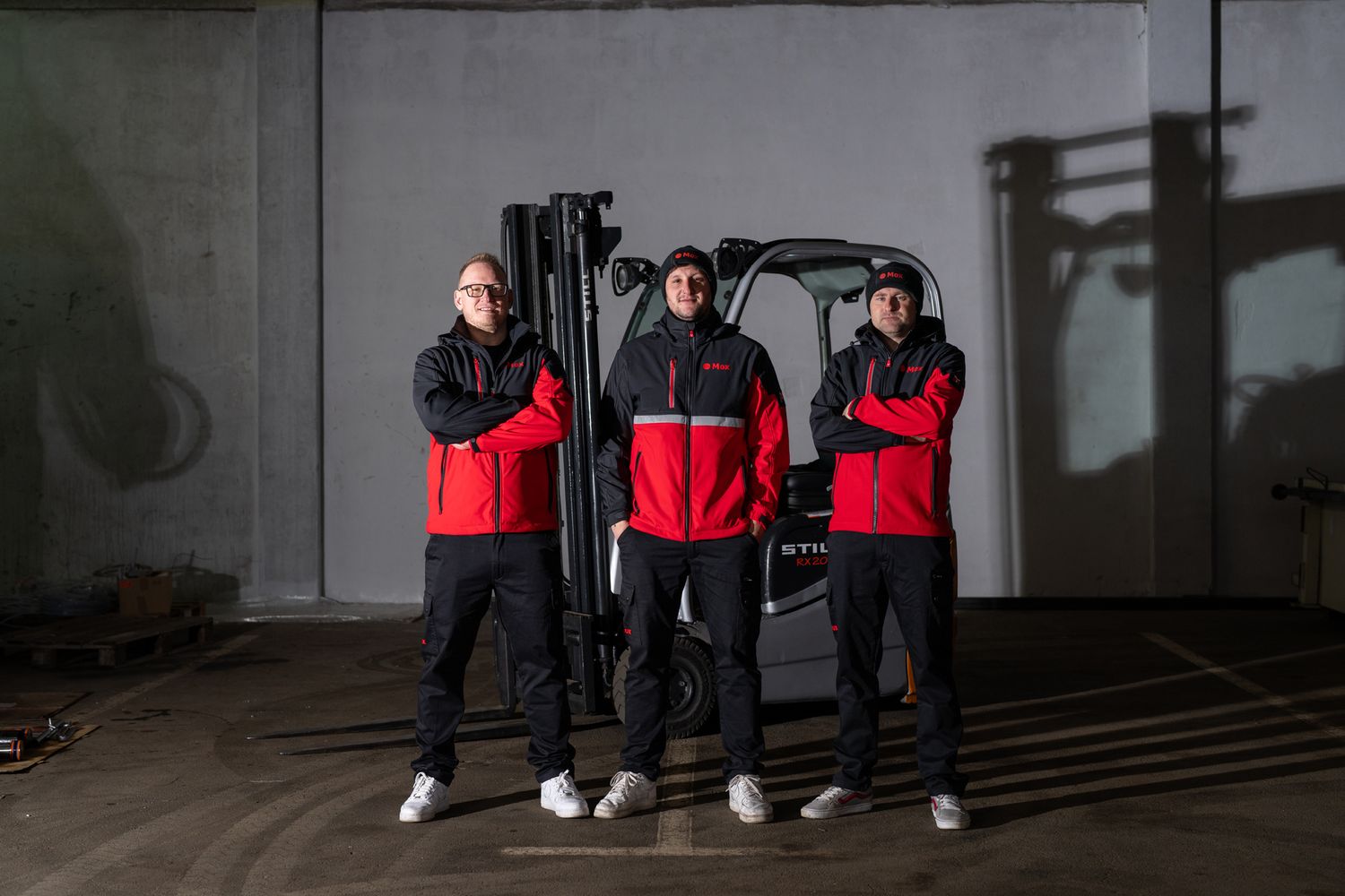 Dance crew in coordinated red and black uniforms posing against concrete wall.
