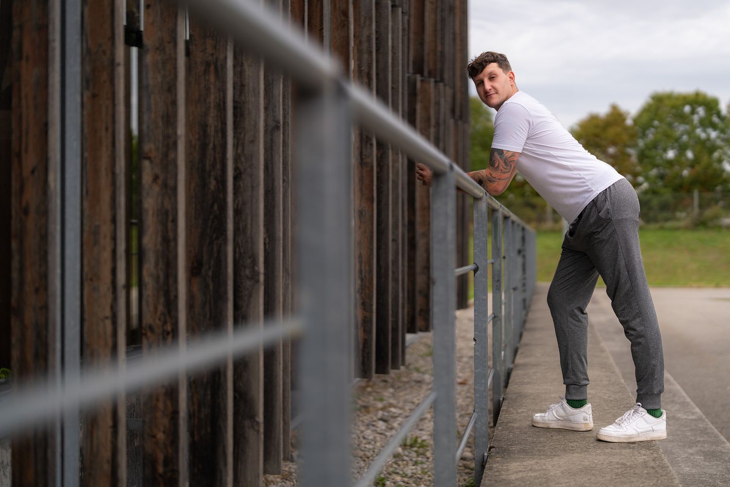 Person in white shirt and gray pants stands near weathered wooden structure.