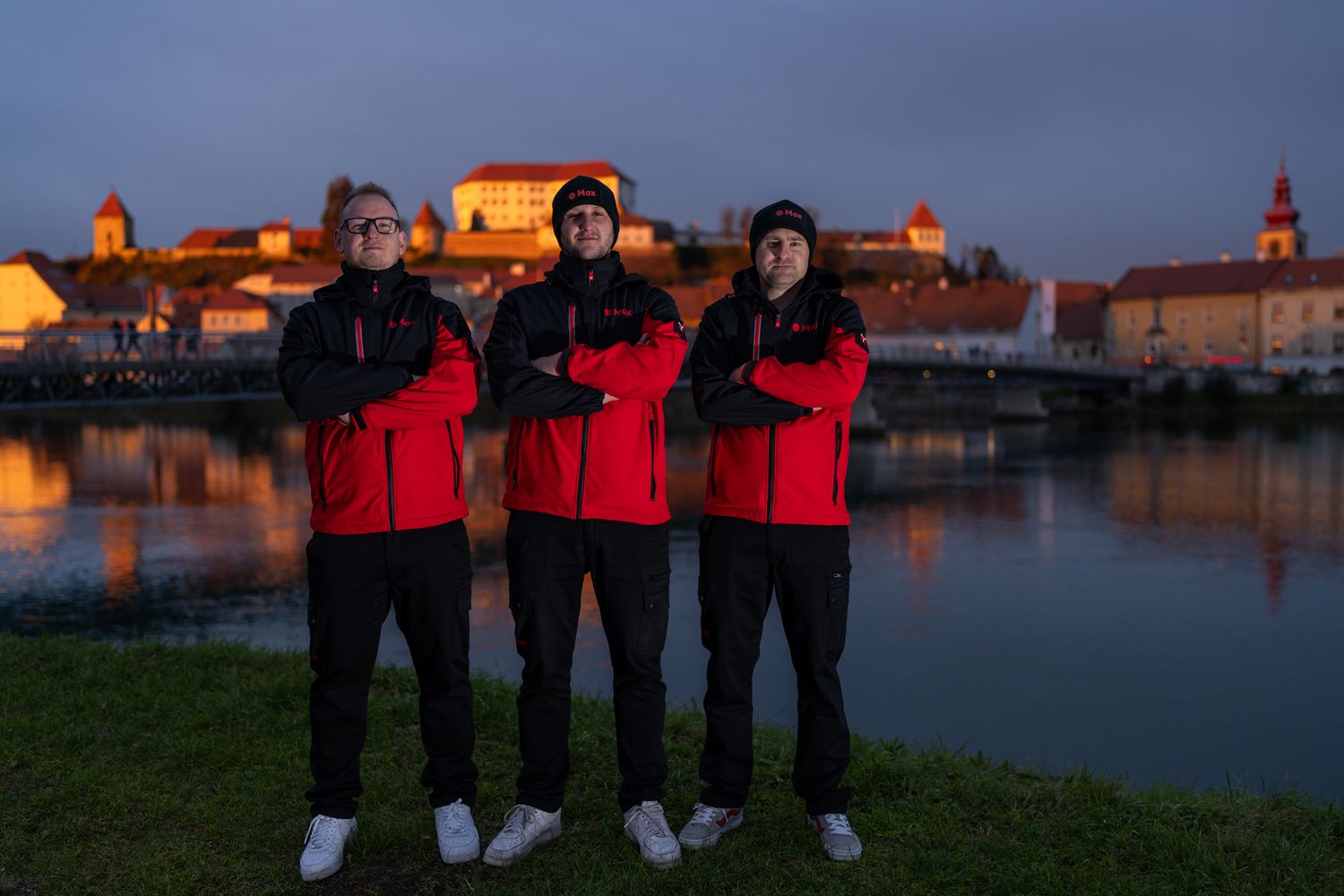 Team wearing matching red jackets posing by waterfront at sunset.