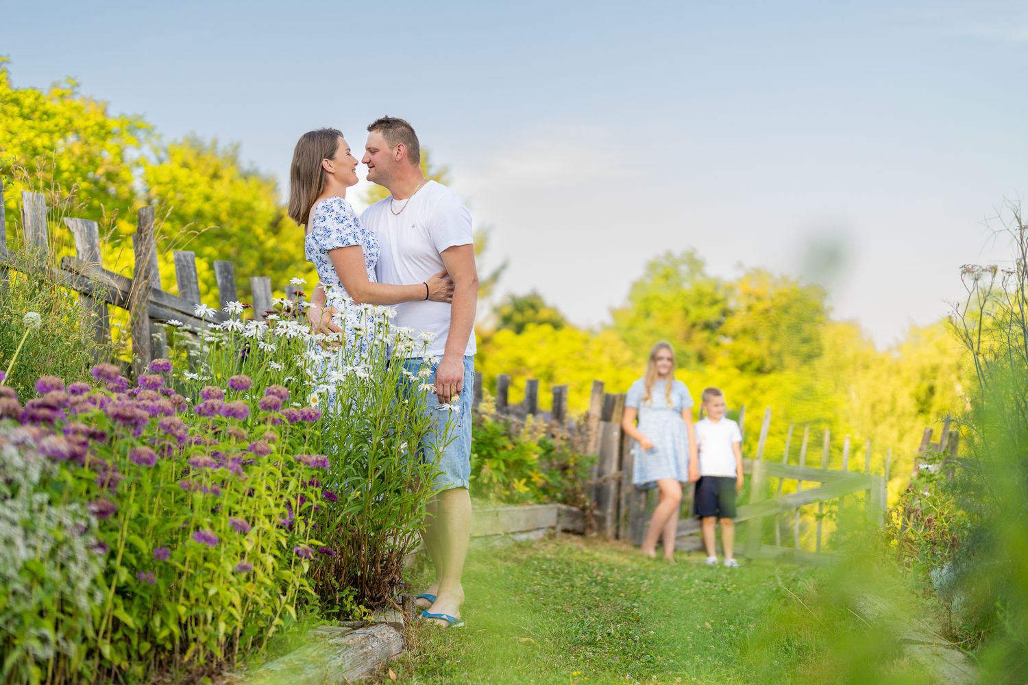 A couple shares a romantic moment in a lush green garden setting during golden hour.