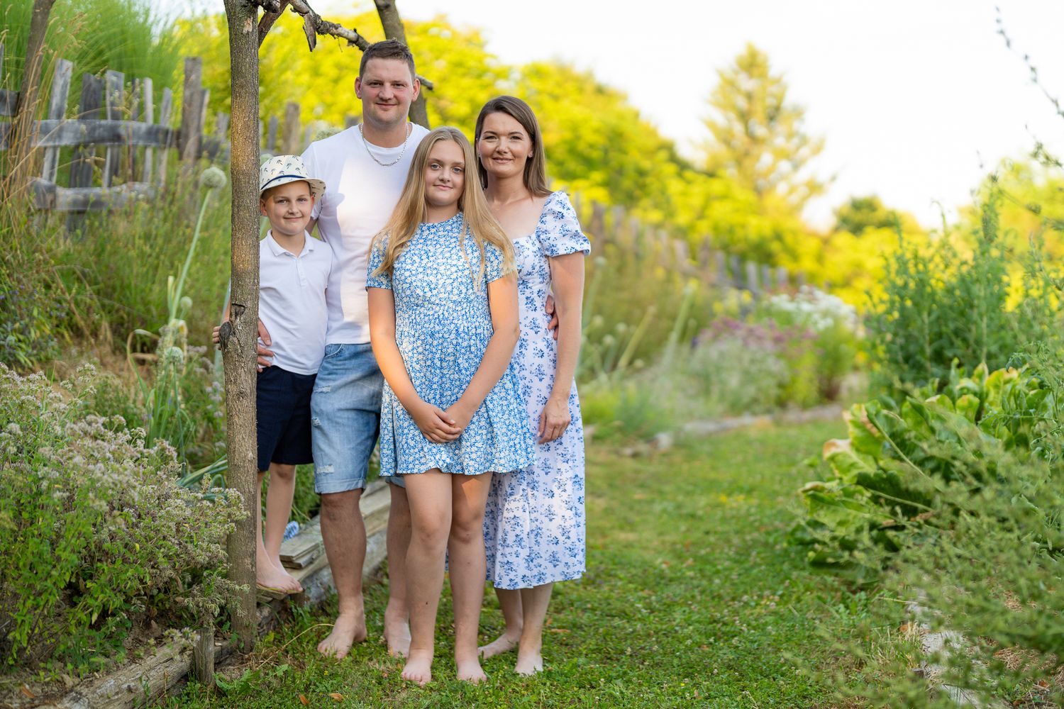 A group stands together in a lush green outdoor setting during golden hour, wearing coordinated blue and white outfits.