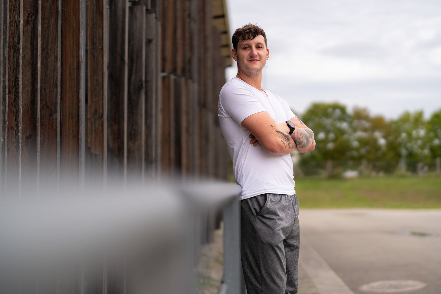 Person in casual attire poses against rustic wooden wall in outdoor setting.