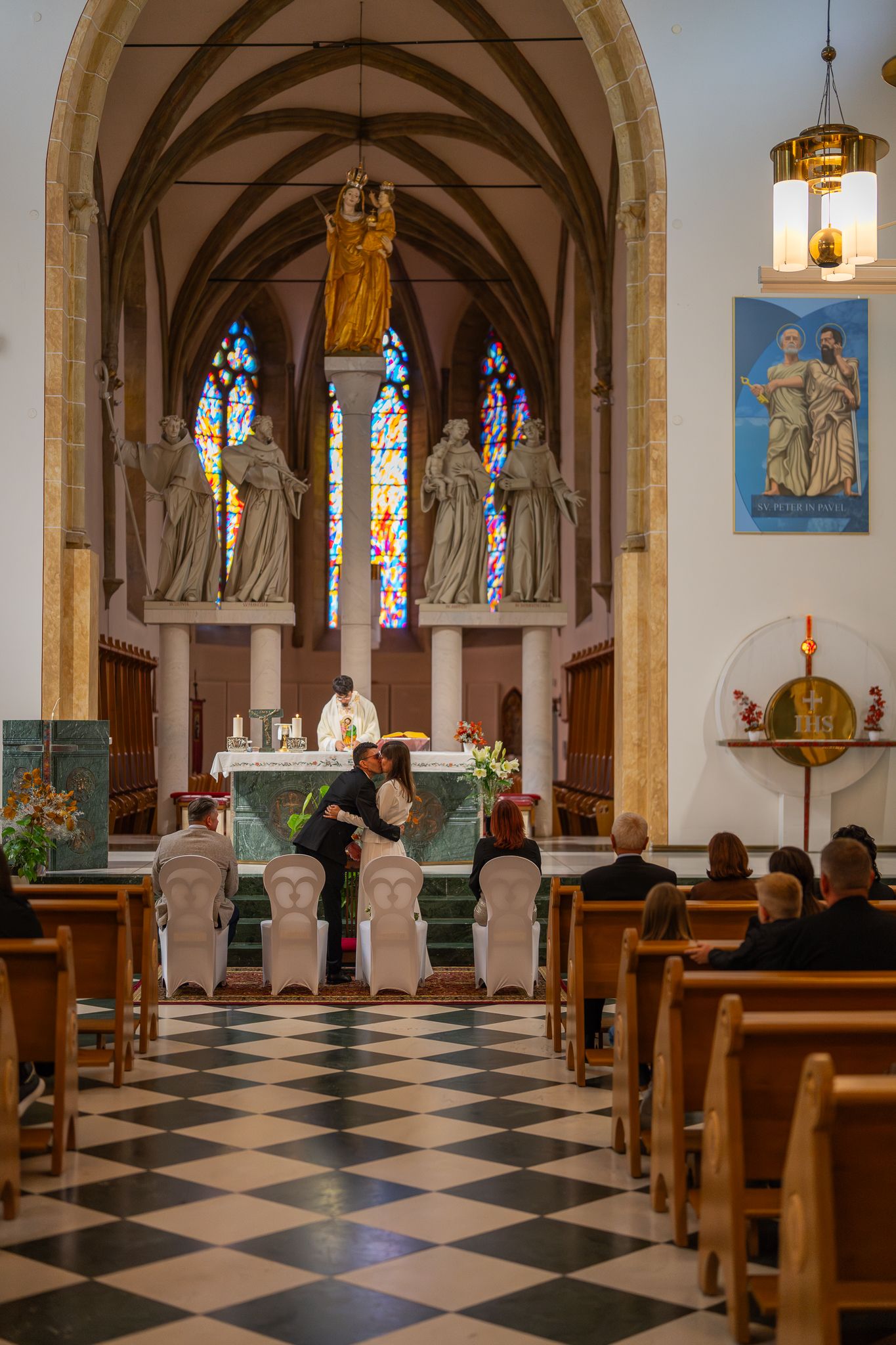 Interior of a historic church with checkered floor and vaulted ceiling adorned with stained glass windows.