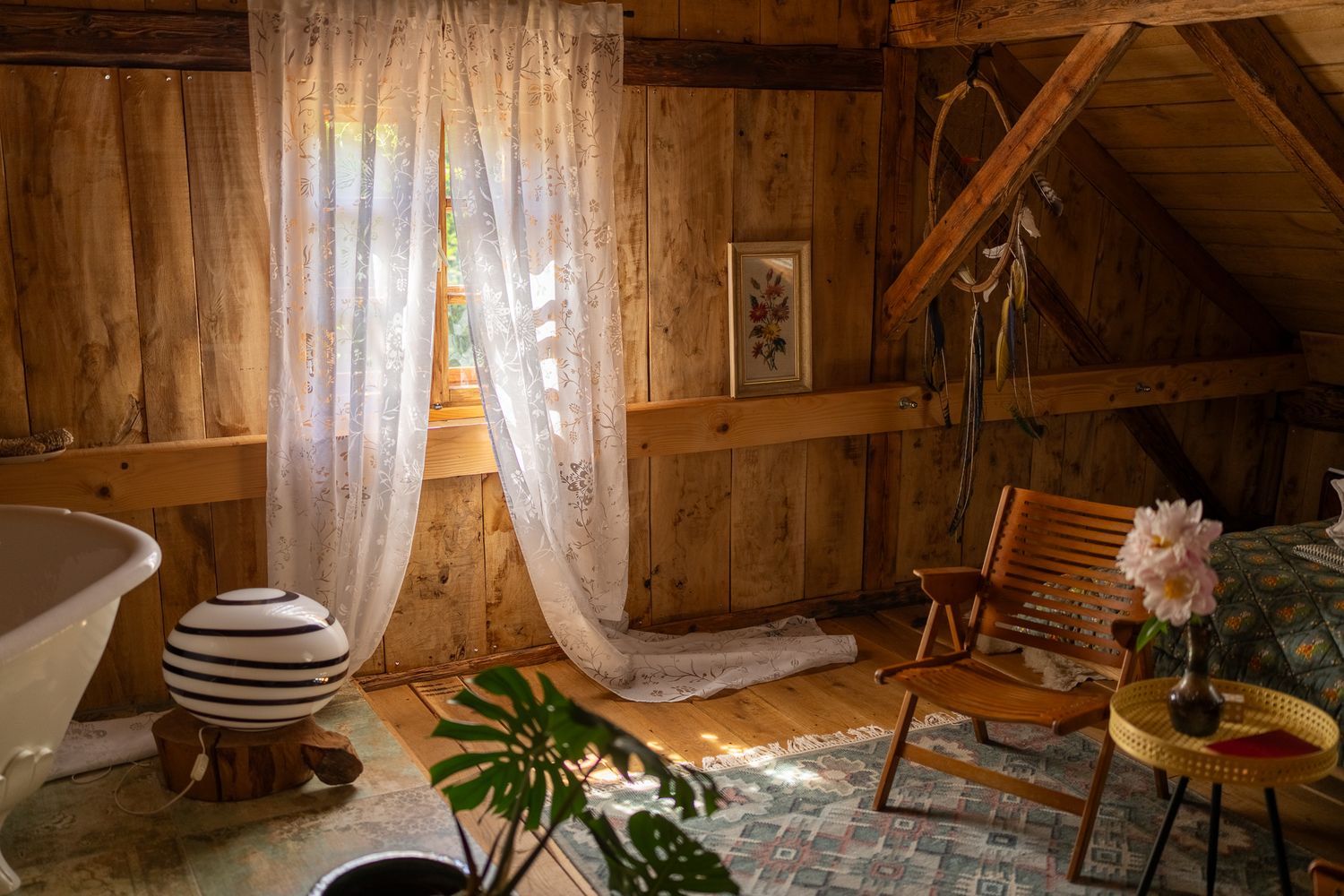 Sunlit cabin living space with wooden furniture and white curtains filtering natural light.