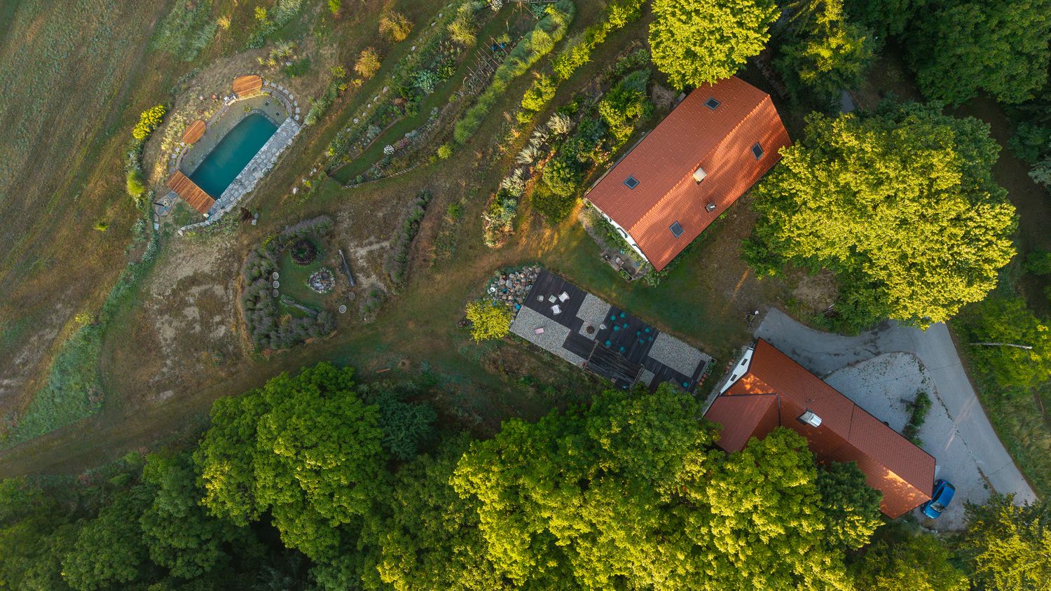 Drone shot of countryside property with swimming pool surrounded by verdant forest.