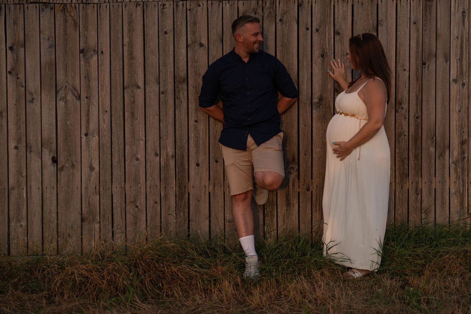 Romantic photoshoot against rustic wooden fence at sunset.