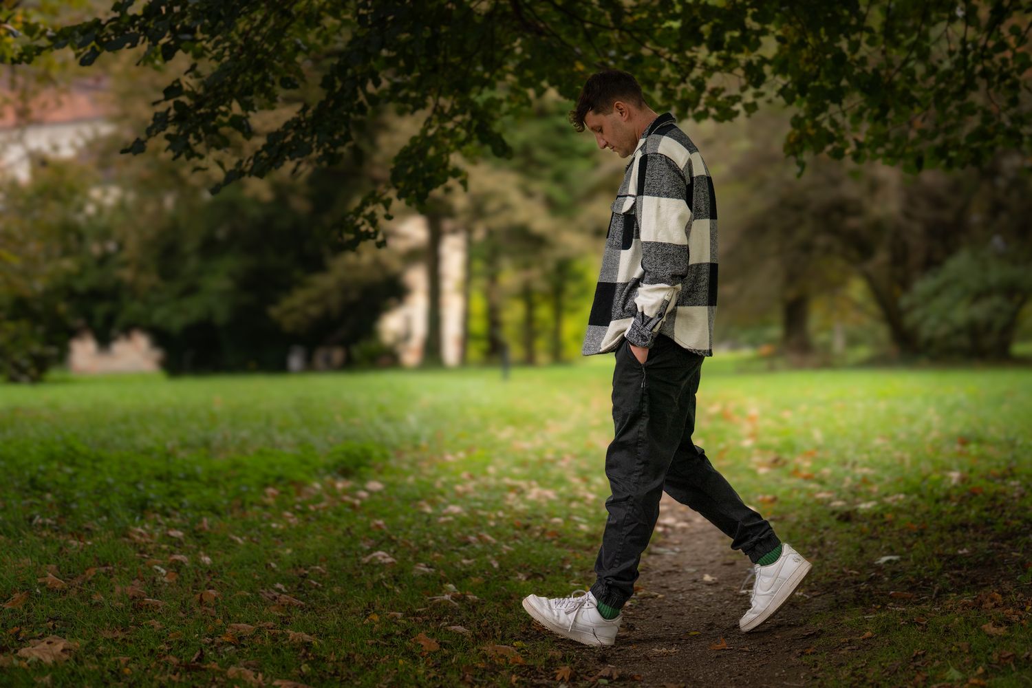 Figure in casual wear and white sneakers walking through park with fallen leaves.