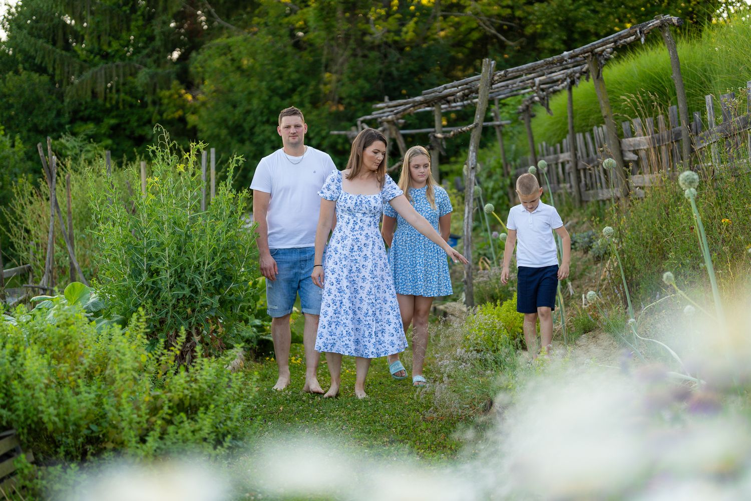 A group stands together in a lush summer garden with wooden fencing and greenery in the background.
