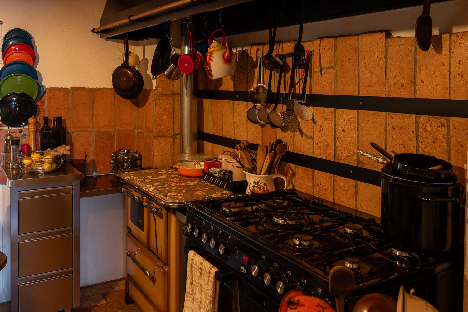 Professional kitchen interior with industrial stove and copper pots hanging overhead.