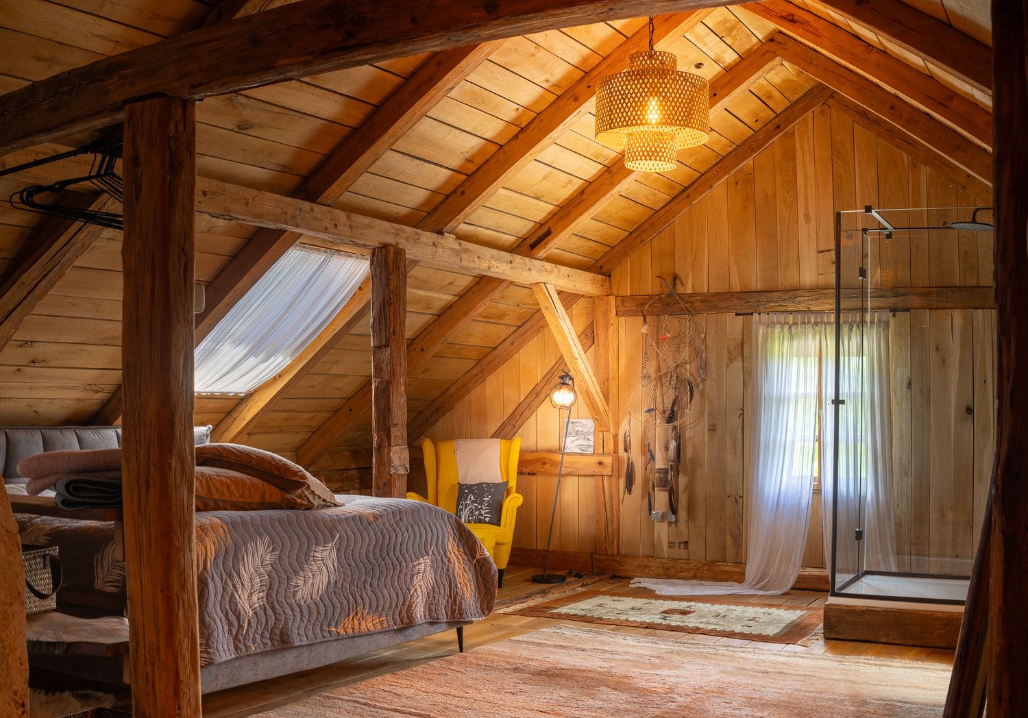 Rustic attic bedroom with exposed wooden beams, glass shower, and sloped ceiling.