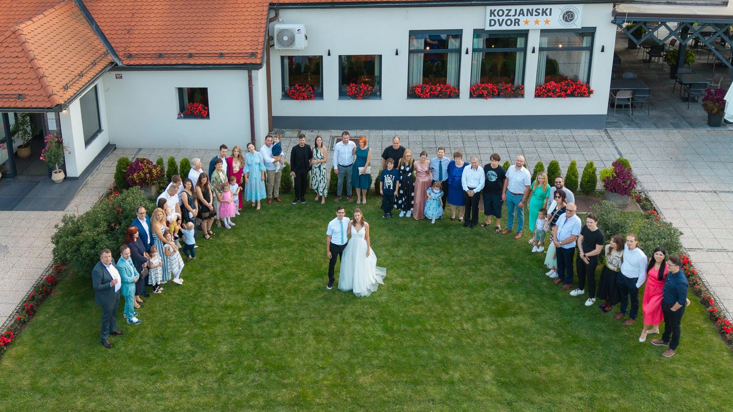 Panoramic shot of wedding guests mingling outside traditional building with red roof.