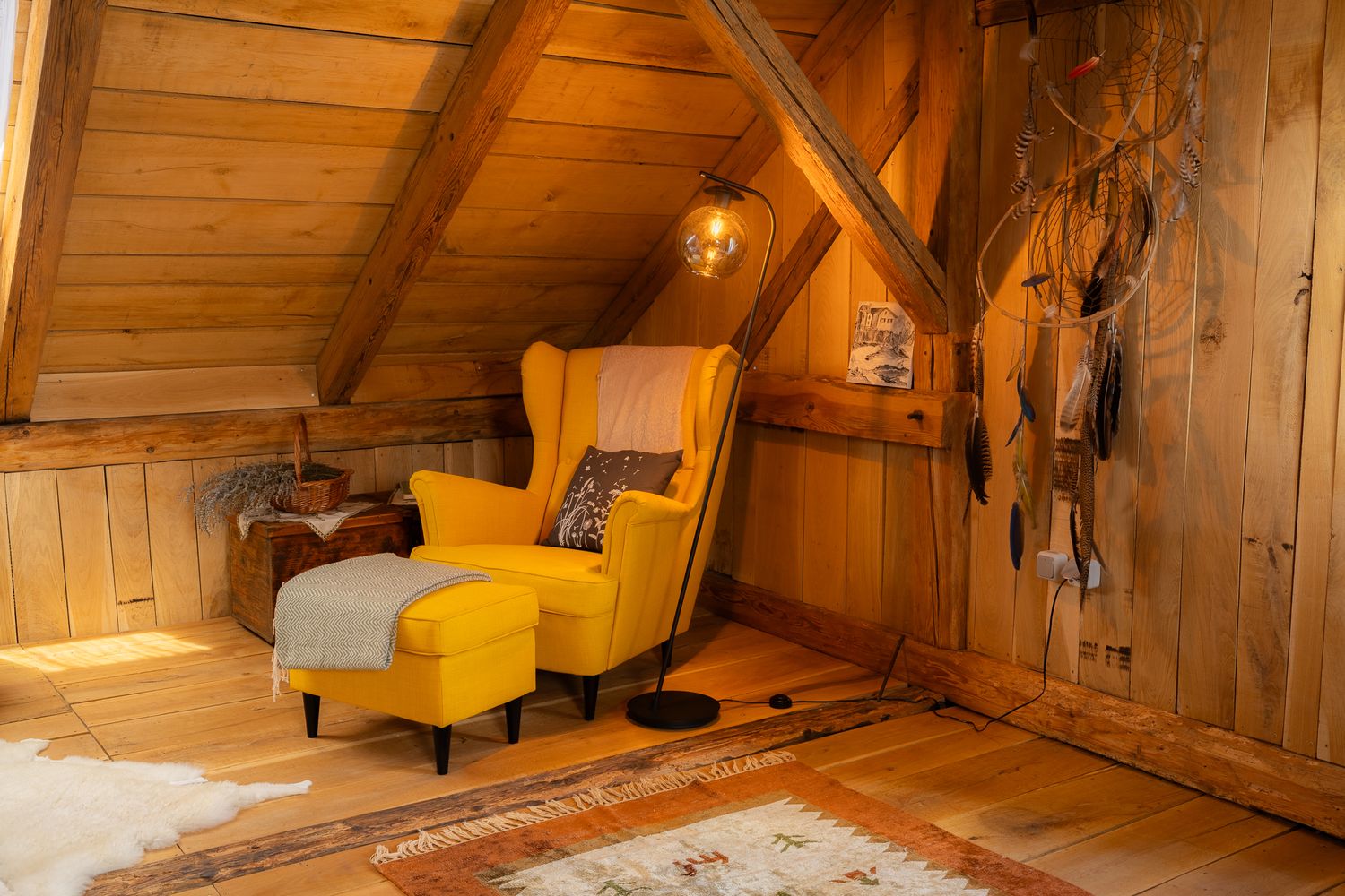 Cozy attic reading nook with yellow armchair and ottoman set against wood-paneled walls.