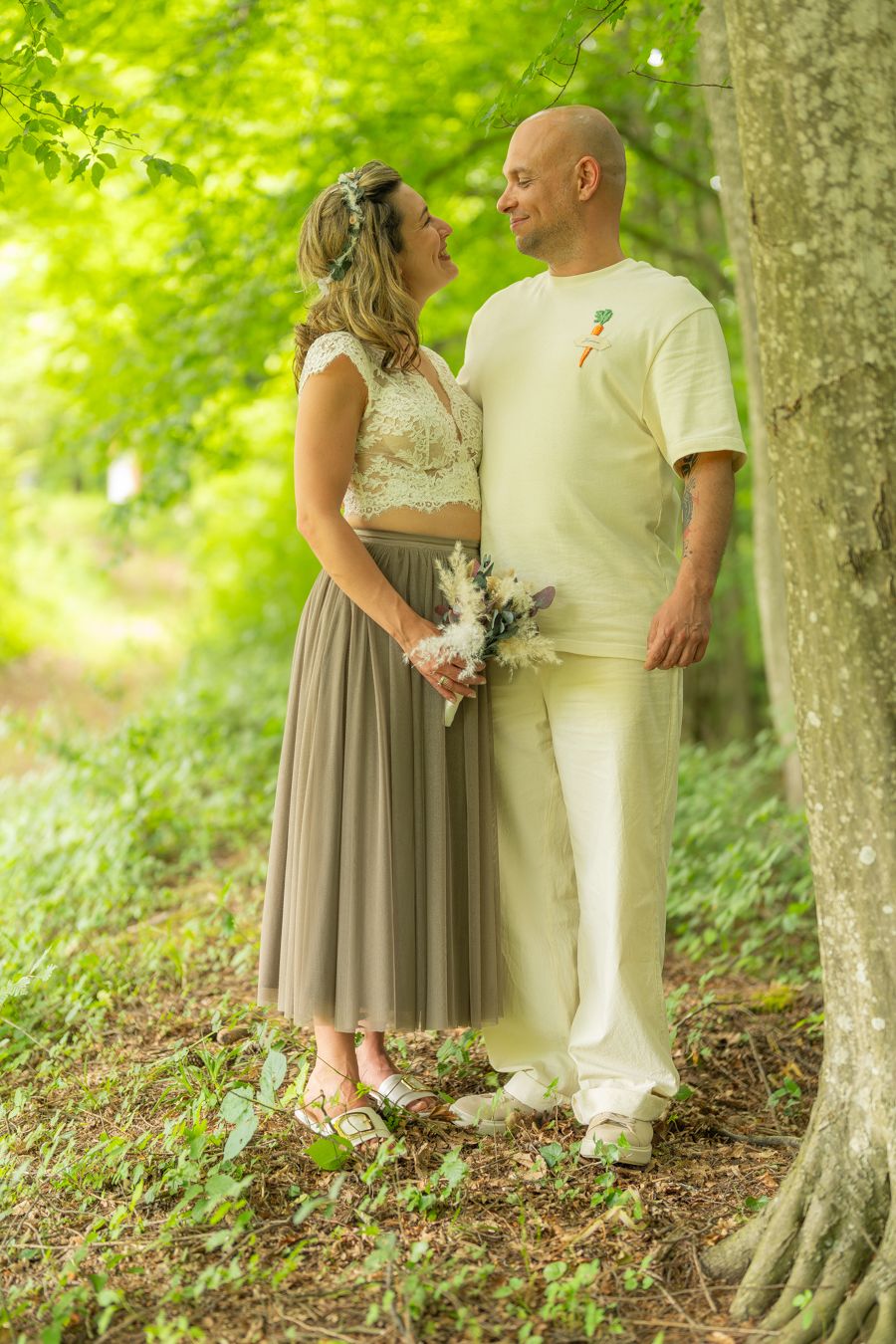 Couple in wedding attire sharing a romantic moment in a lush green forest, woman holding a bouquet.