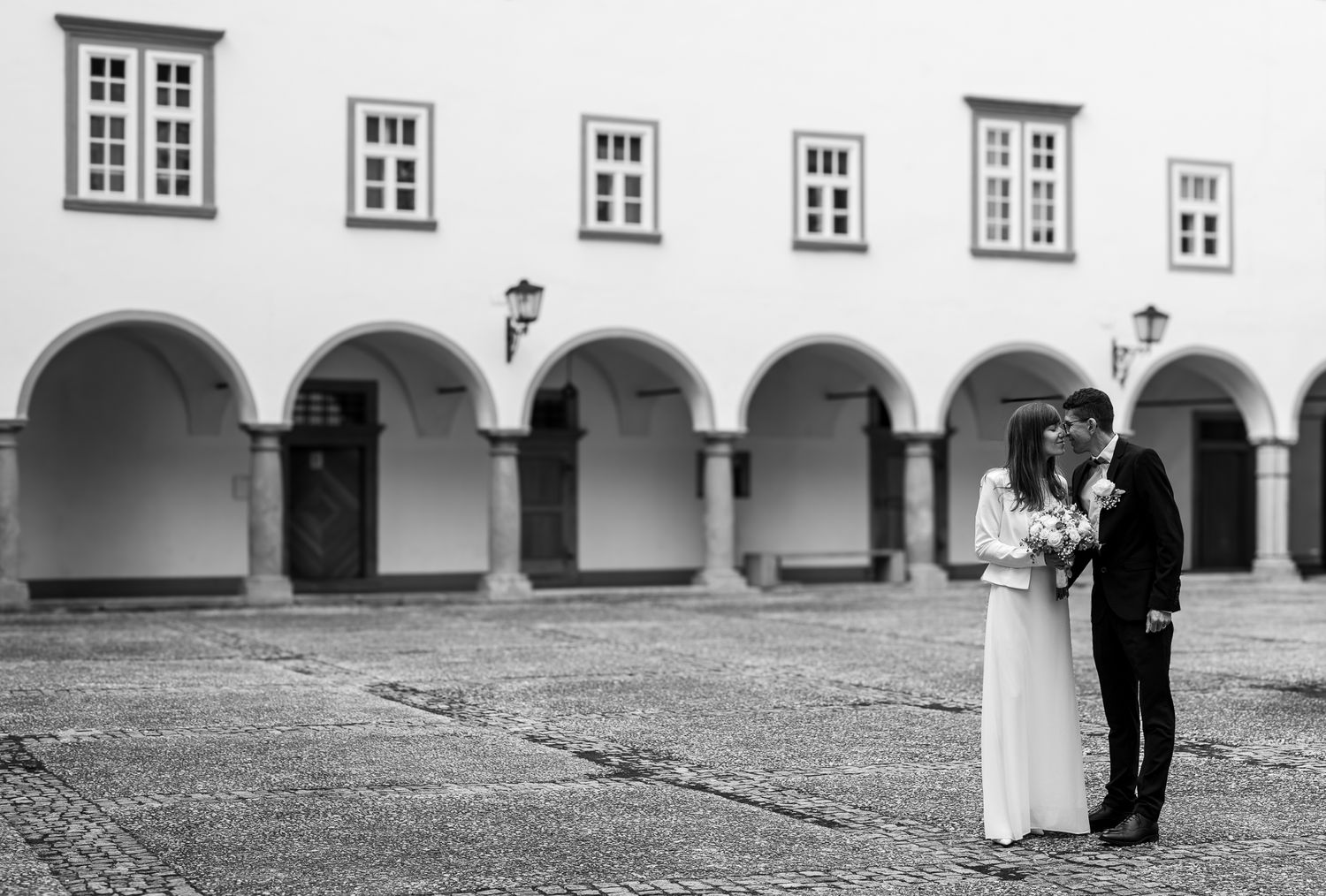 A series of black and white wedding photos showing couples in elegant poses under arched walkways and courtyards.