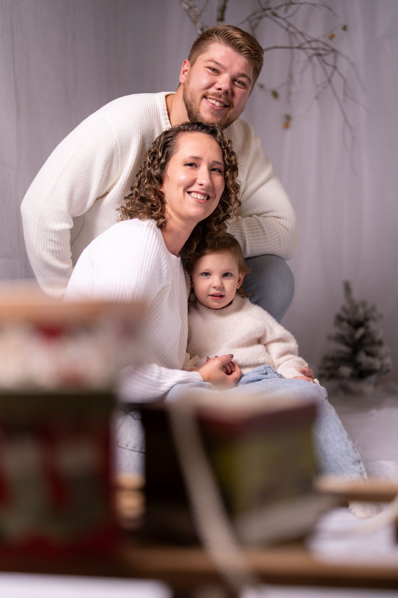 Family poses together wearing white sweaters in a cozy winter photoshoot.