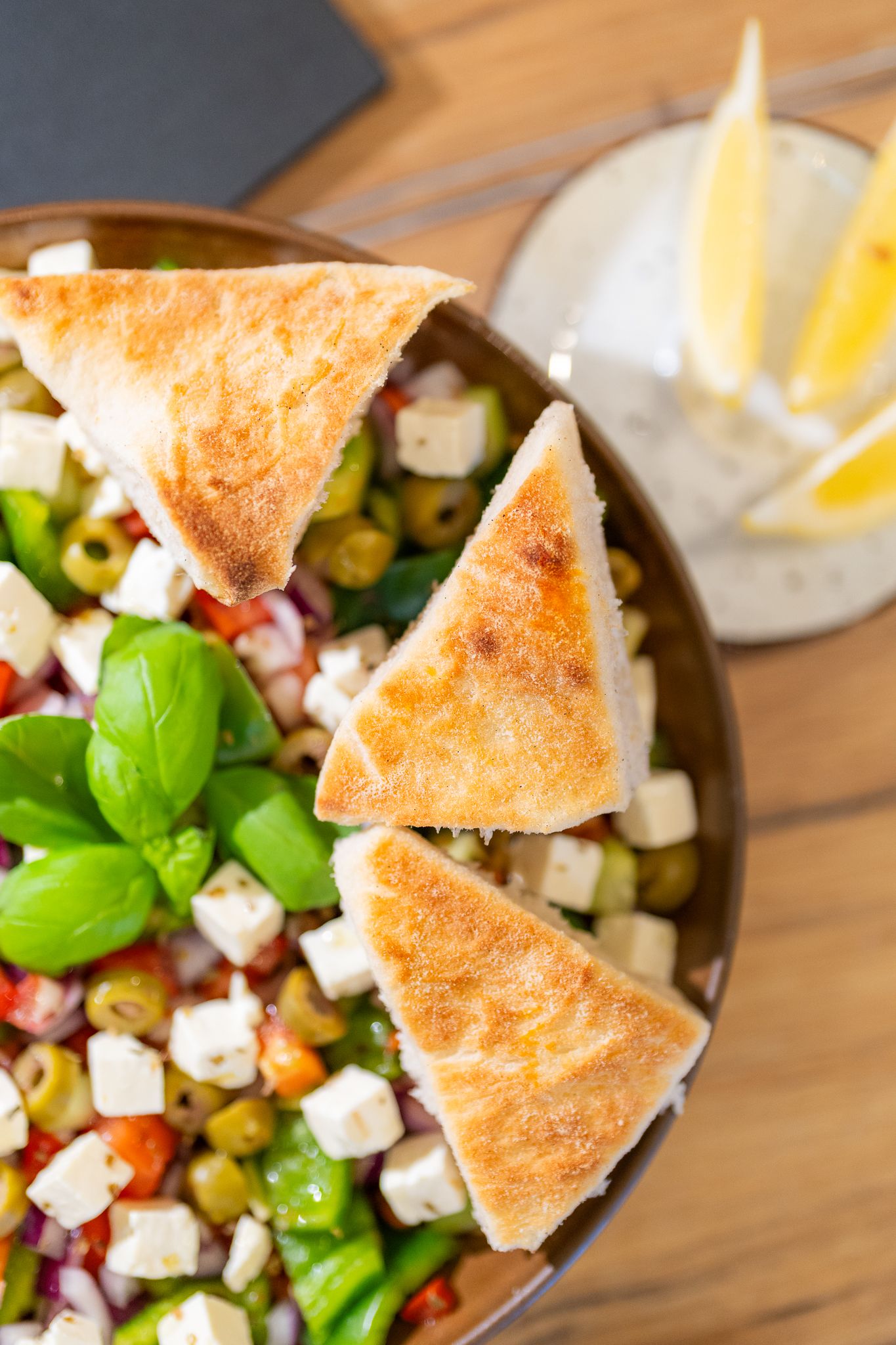Fresh Mediterranean salad with feta cheese, olives and pita bread triangles in wooden bowl.