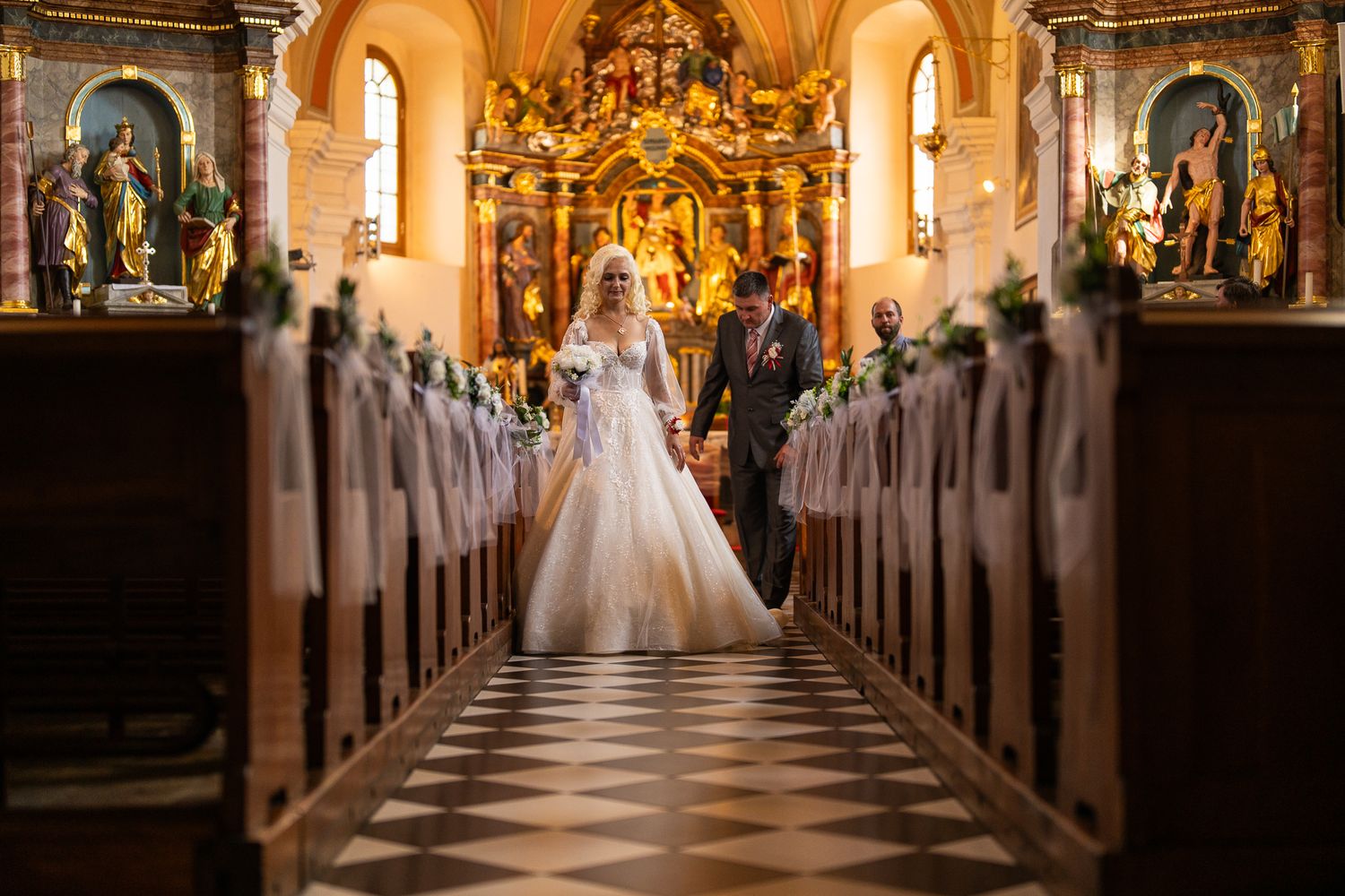 Elegant church interior with ornate gold altar and long aisle during wedding ceremony.