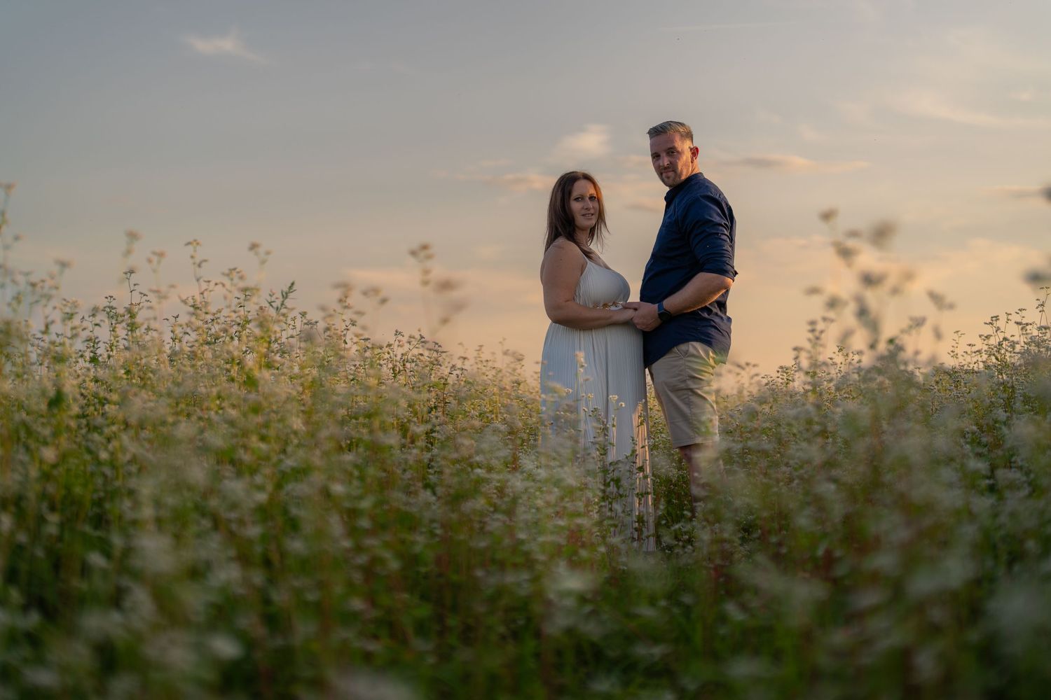 Couple standing in a wildflower field during golden sunset.