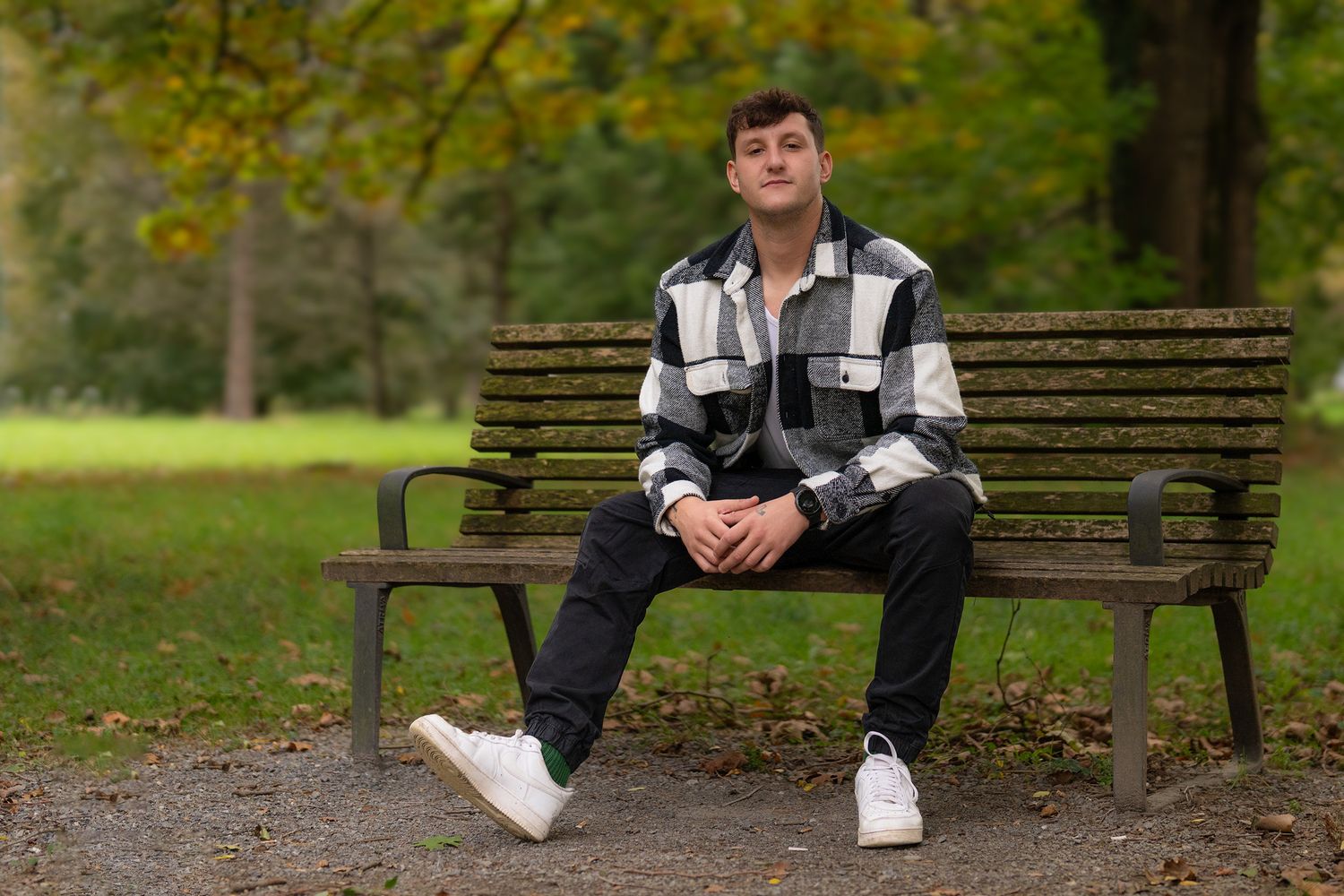 Person sitting on wooden bench in park during autumn season.