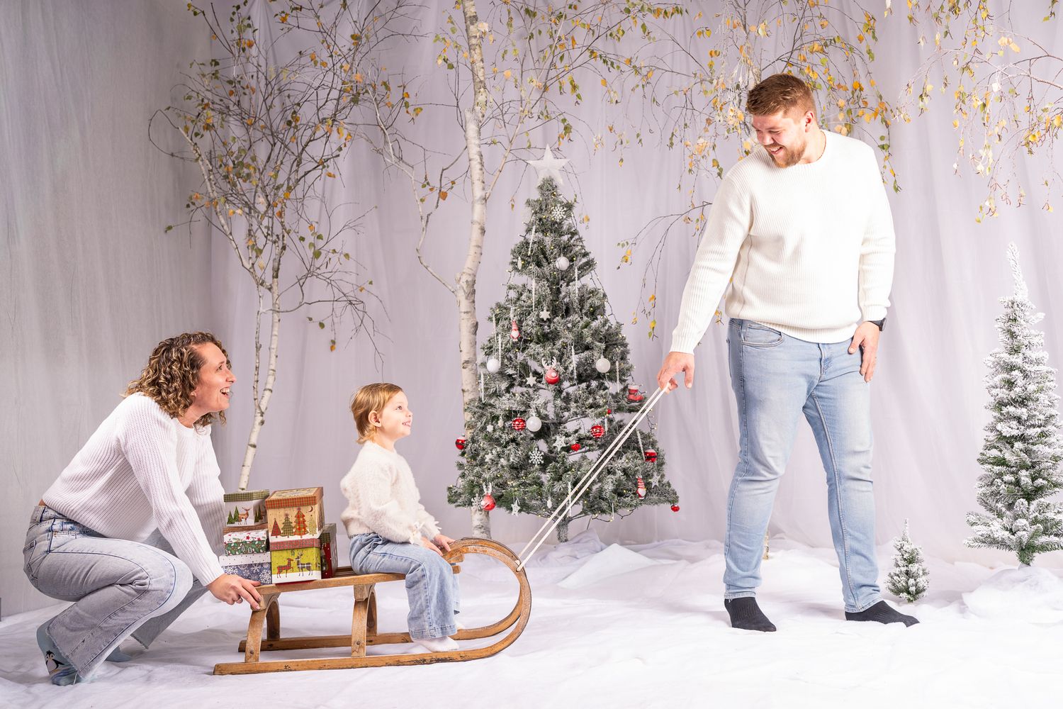 Winter themed photoshoot with decorative trees and holiday decor in a bright studio.