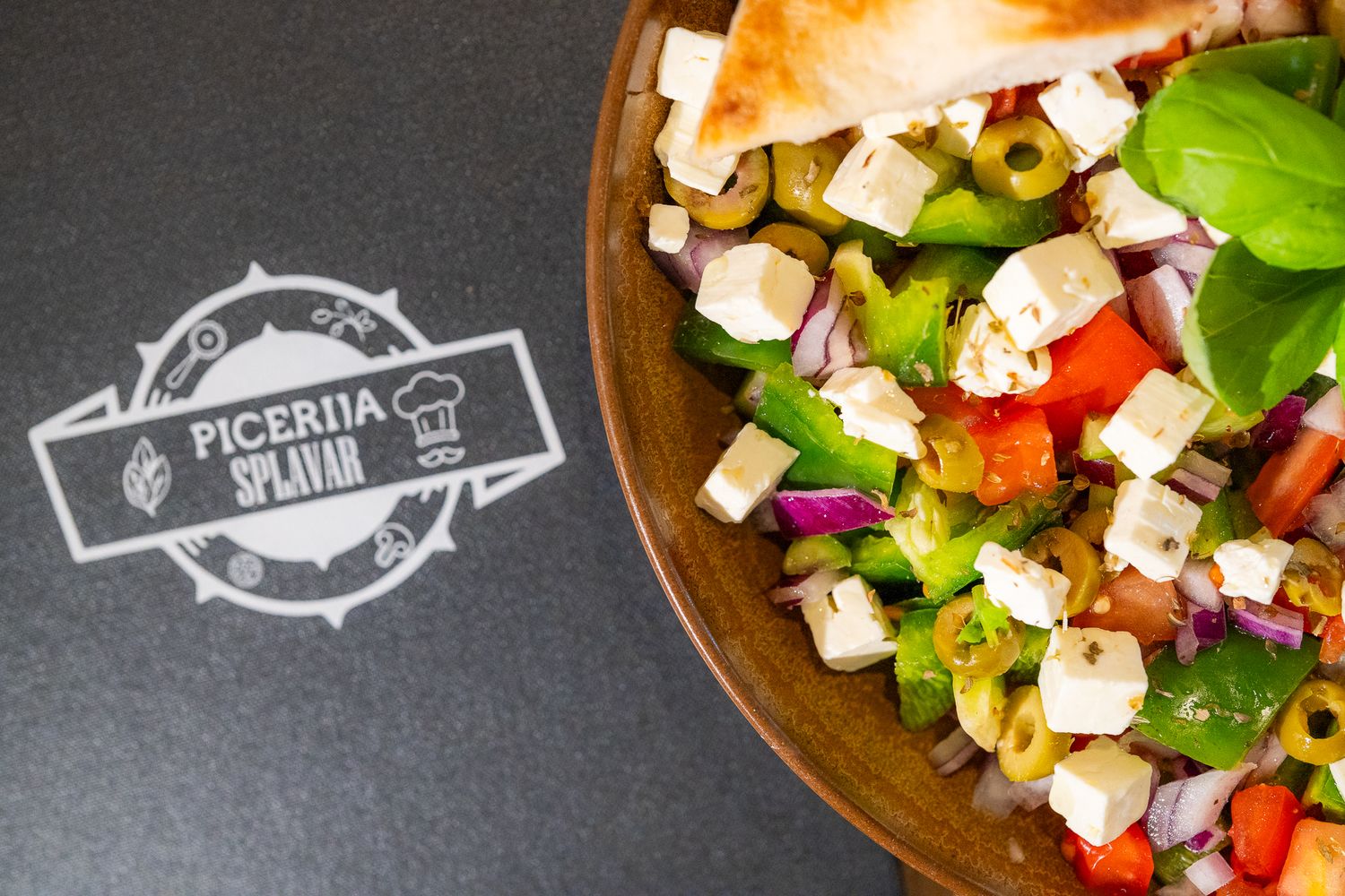 Fresh Greek salad with feta cheese cubes, olives, and vegetables in a wooden bowl.