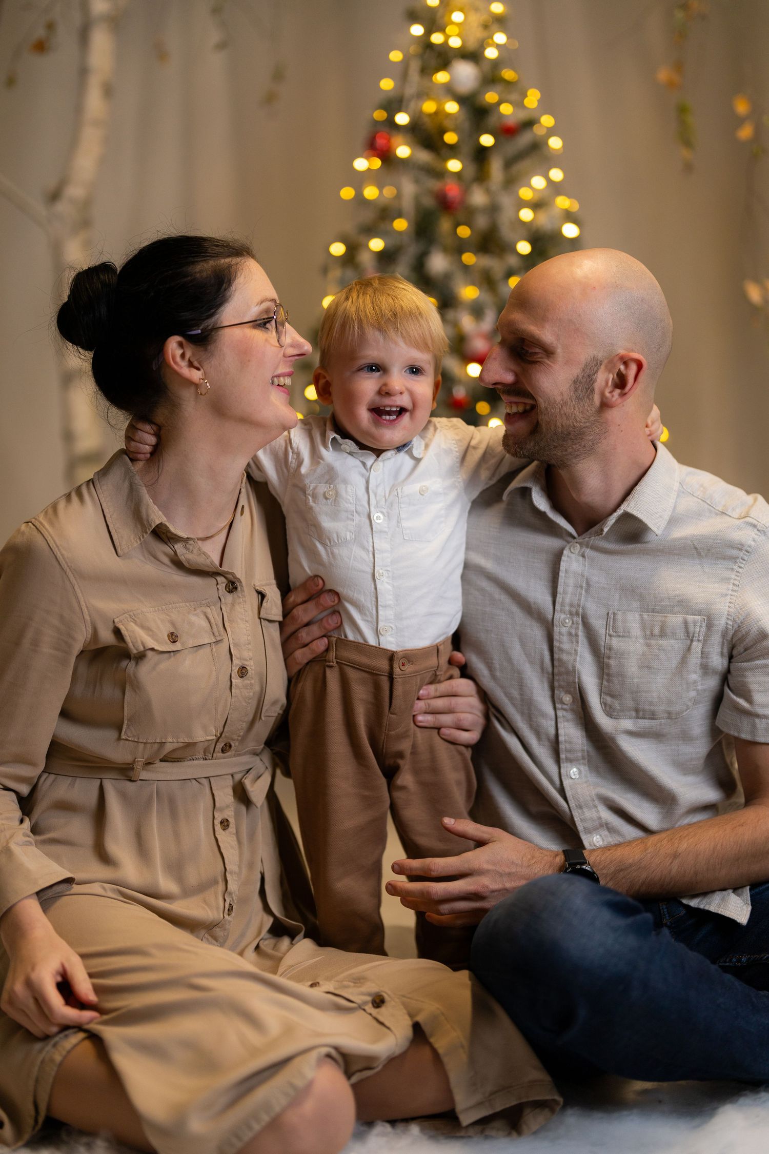 A family shares joyful moments together on a couch with a Christmas tree glowing in the background.