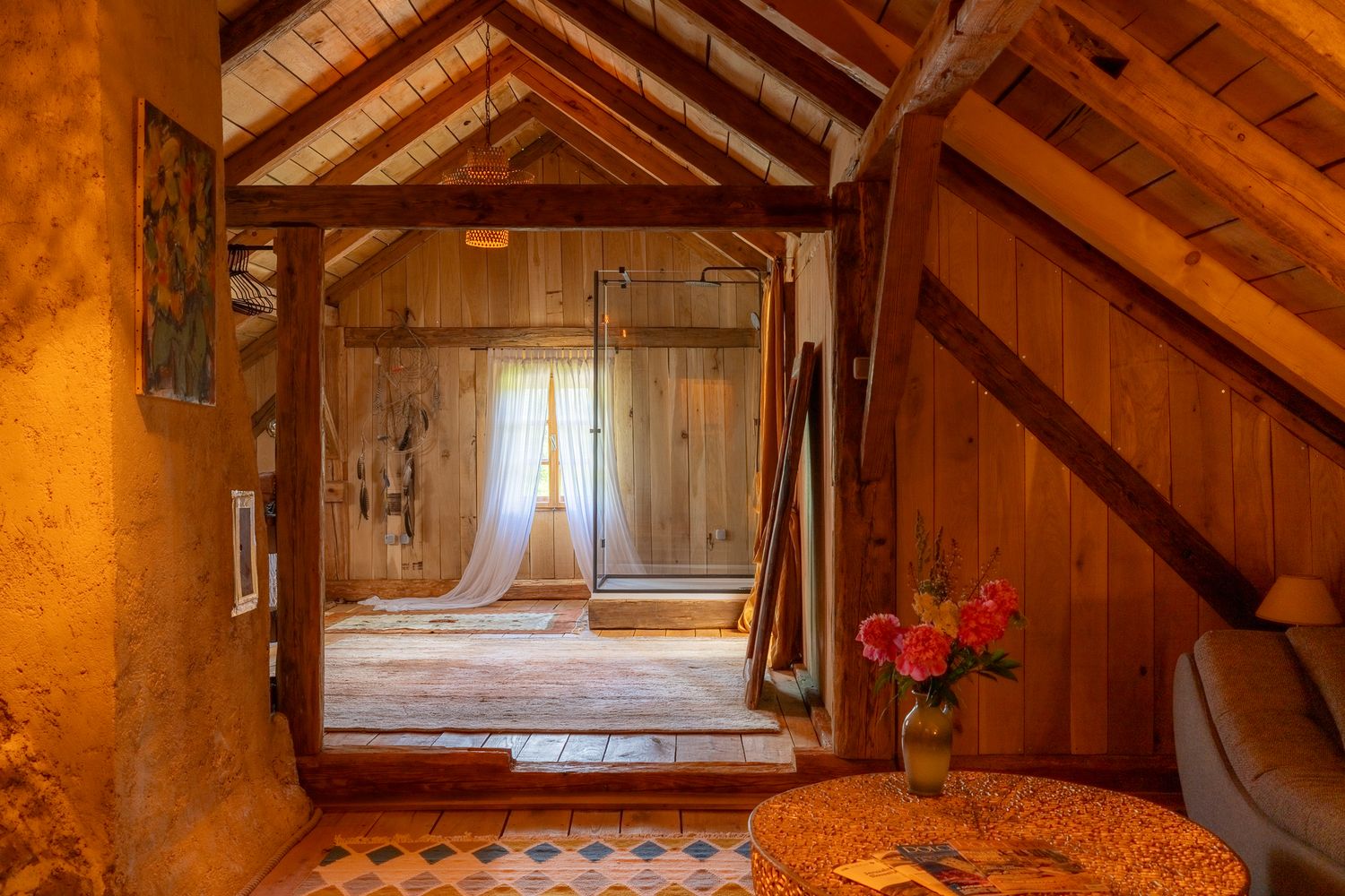 Sunlit attic doorway with wooden panels and red flowers creating a warm, inviting atmosphere.