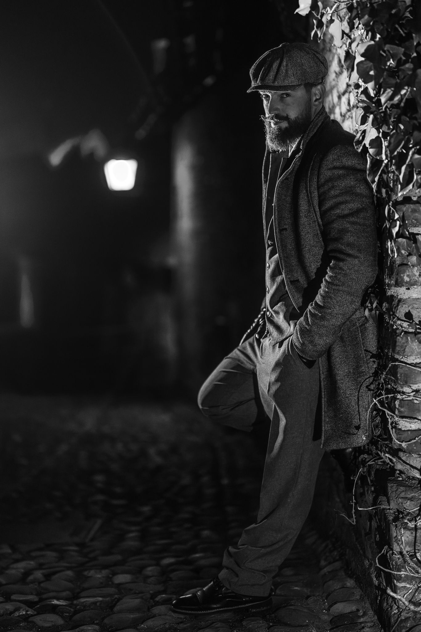 Noir-style black and white portrait of person in vintage attire leaning against wall.