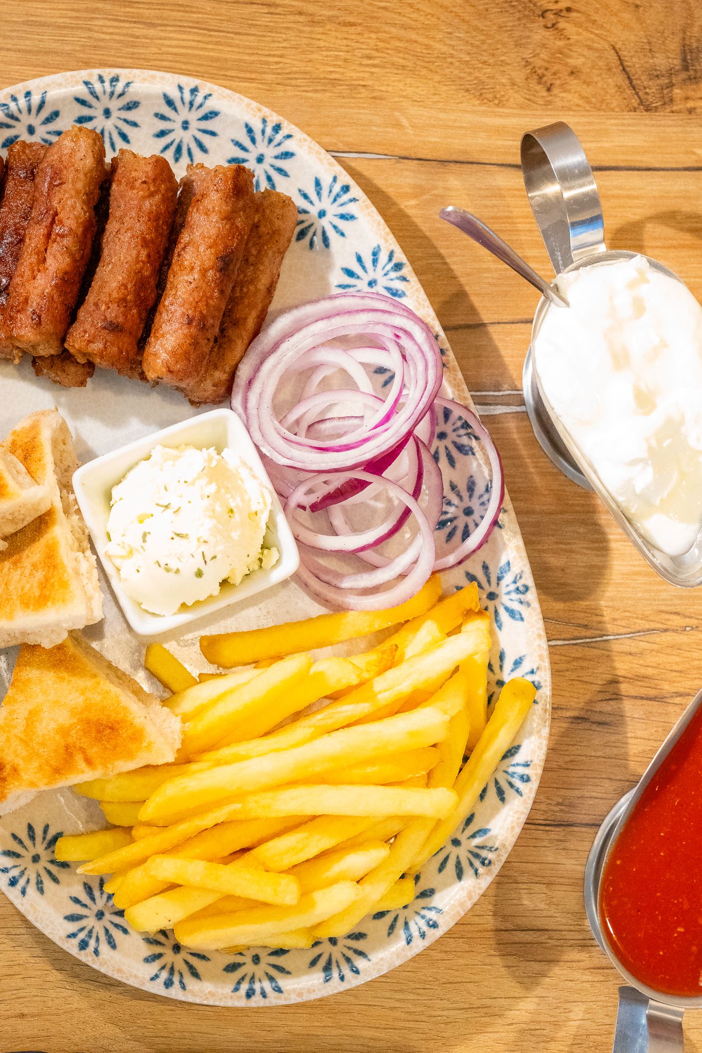 Platter of french fries with onions and dipping sauces served on a decorative plate.