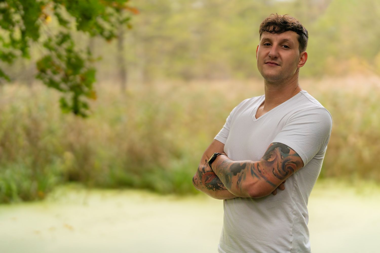 Person in white t-shirt showing tattooed arms in outdoor nature setting.