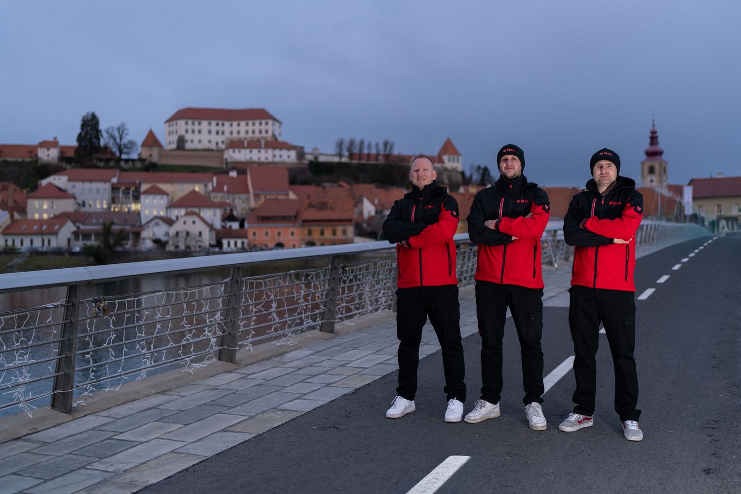 Group in matching red and black outfits standing on a stone bridge at dusk.