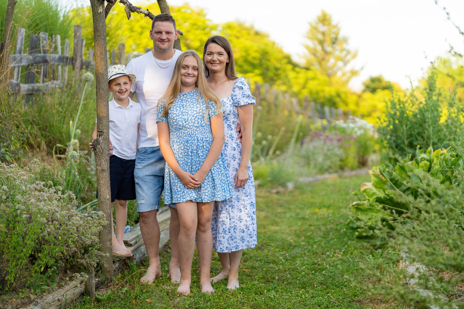 Family group poses together in a lush garden setting during golden hour lighting.