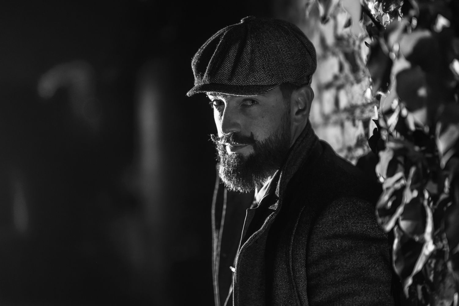 Atmospheric black and white shot of person in vintage clothing against textured wall.
