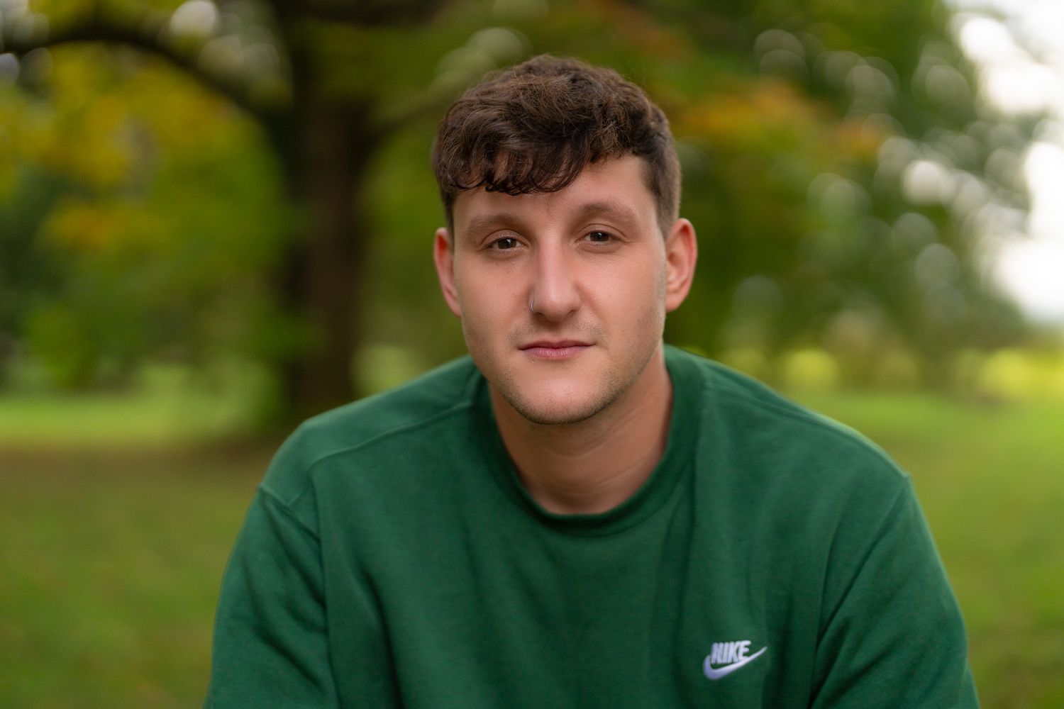 Person wearing green Nike sweatshirt relaxes outdoors in park setting.