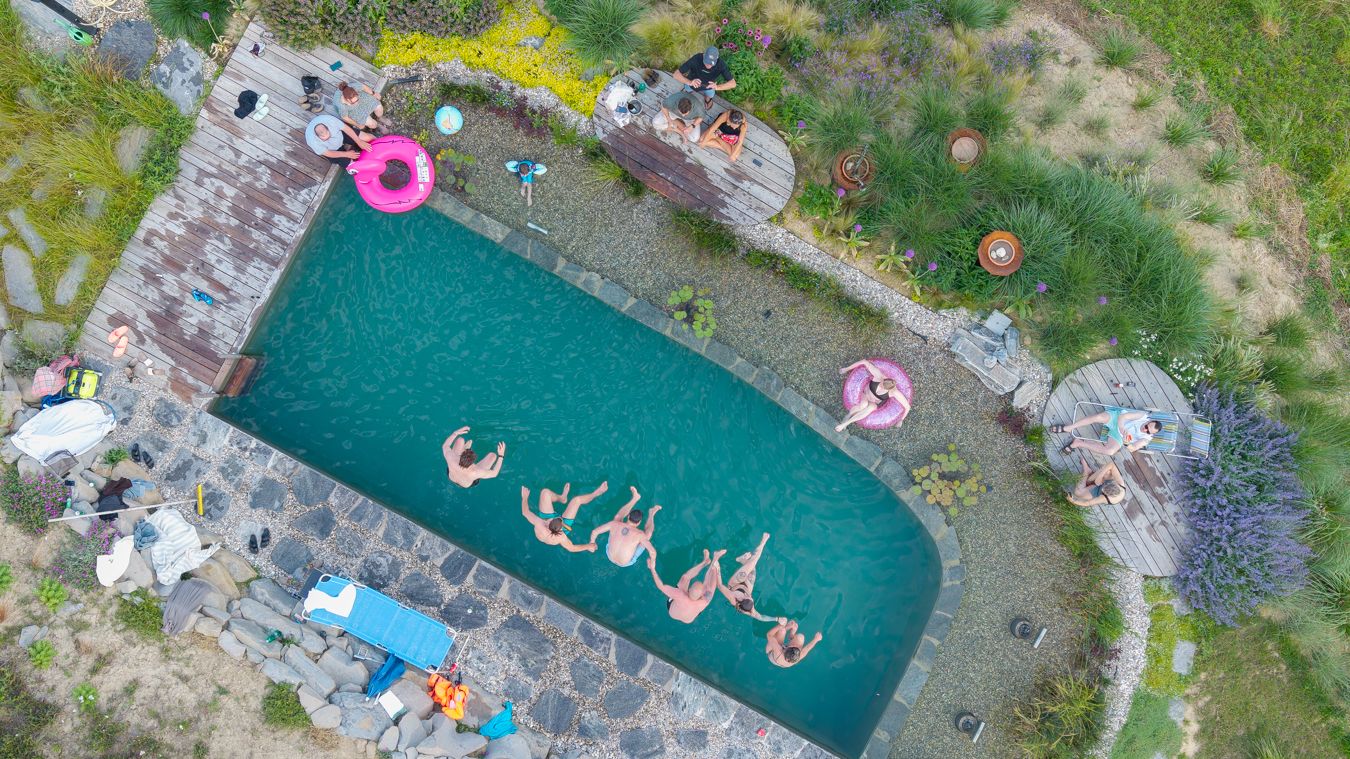 Aerial view of guests floating in a natural stone swimming pool with pink inflatables.