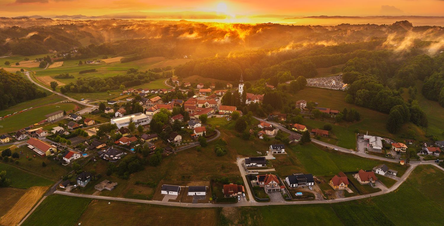 Aerial sunset view of rural village nestled among rolling hills with golden light.