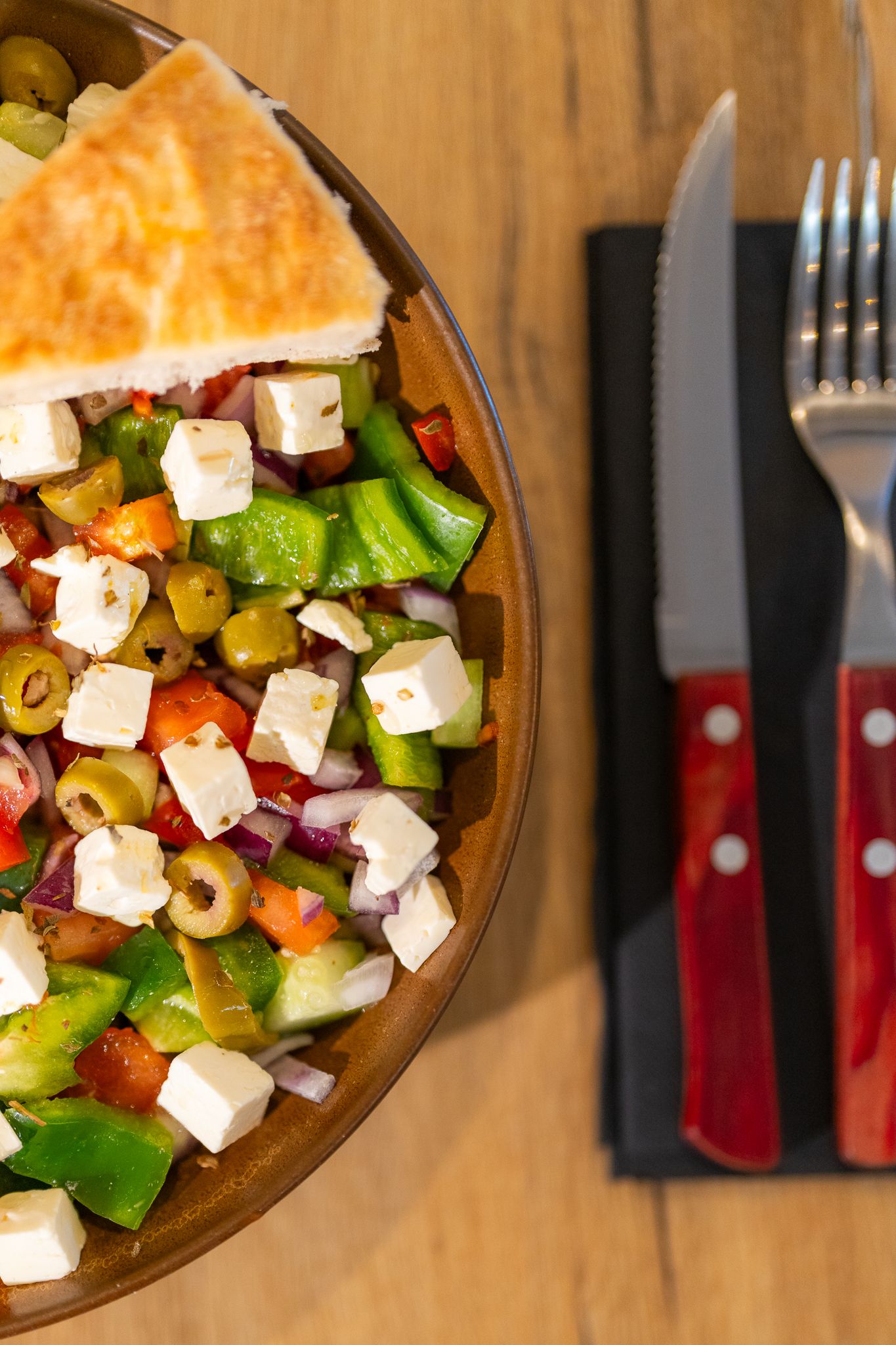 Colorful Mediterranean salad topped with cubed feta cheese and olives in wooden bowl.