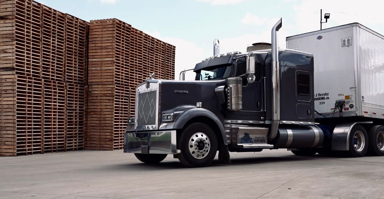 A grey Kenworth semi truck in front of wood pallets