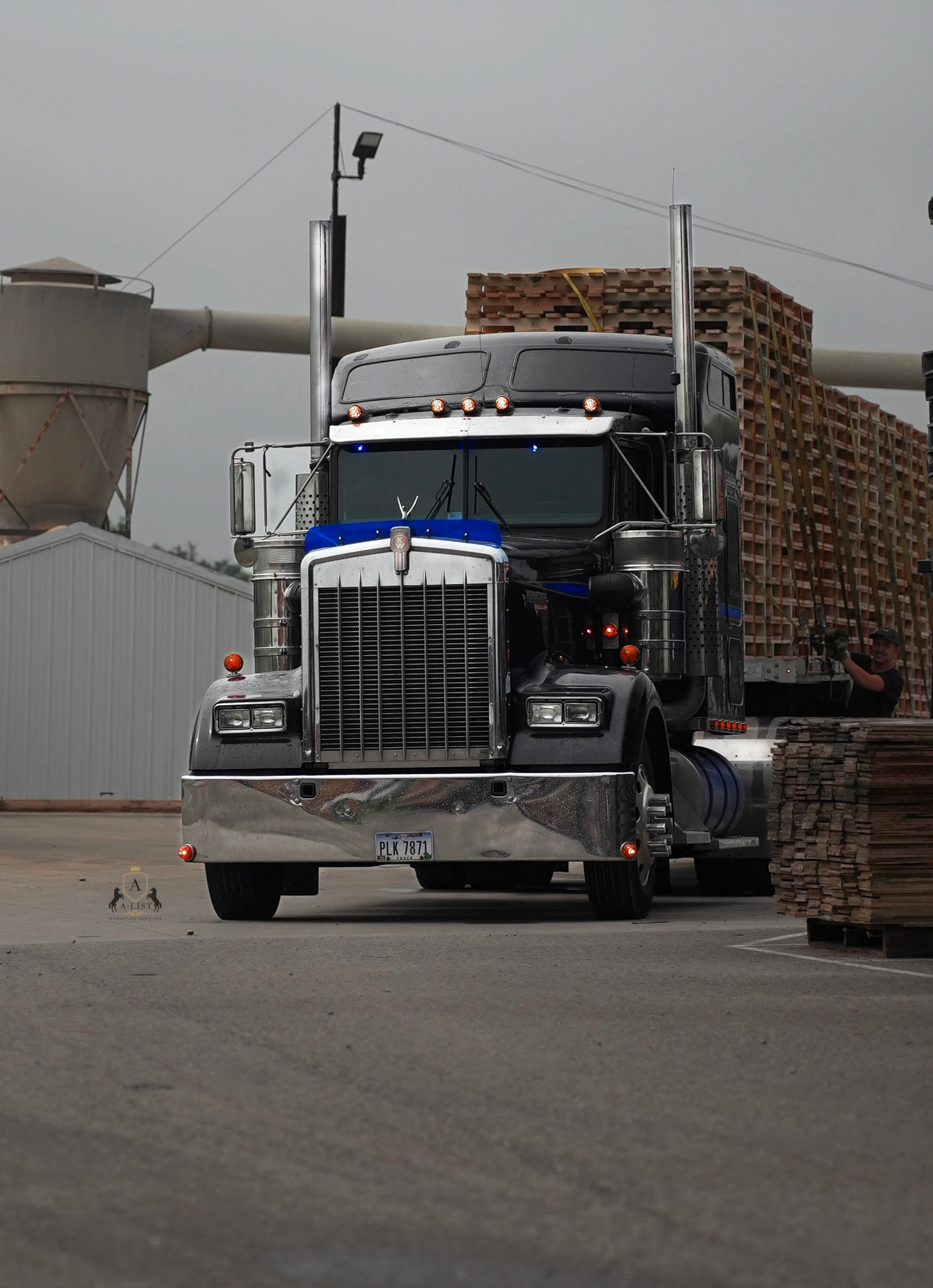 A black and blue Kenworth semi truck with a step deck load of pallets