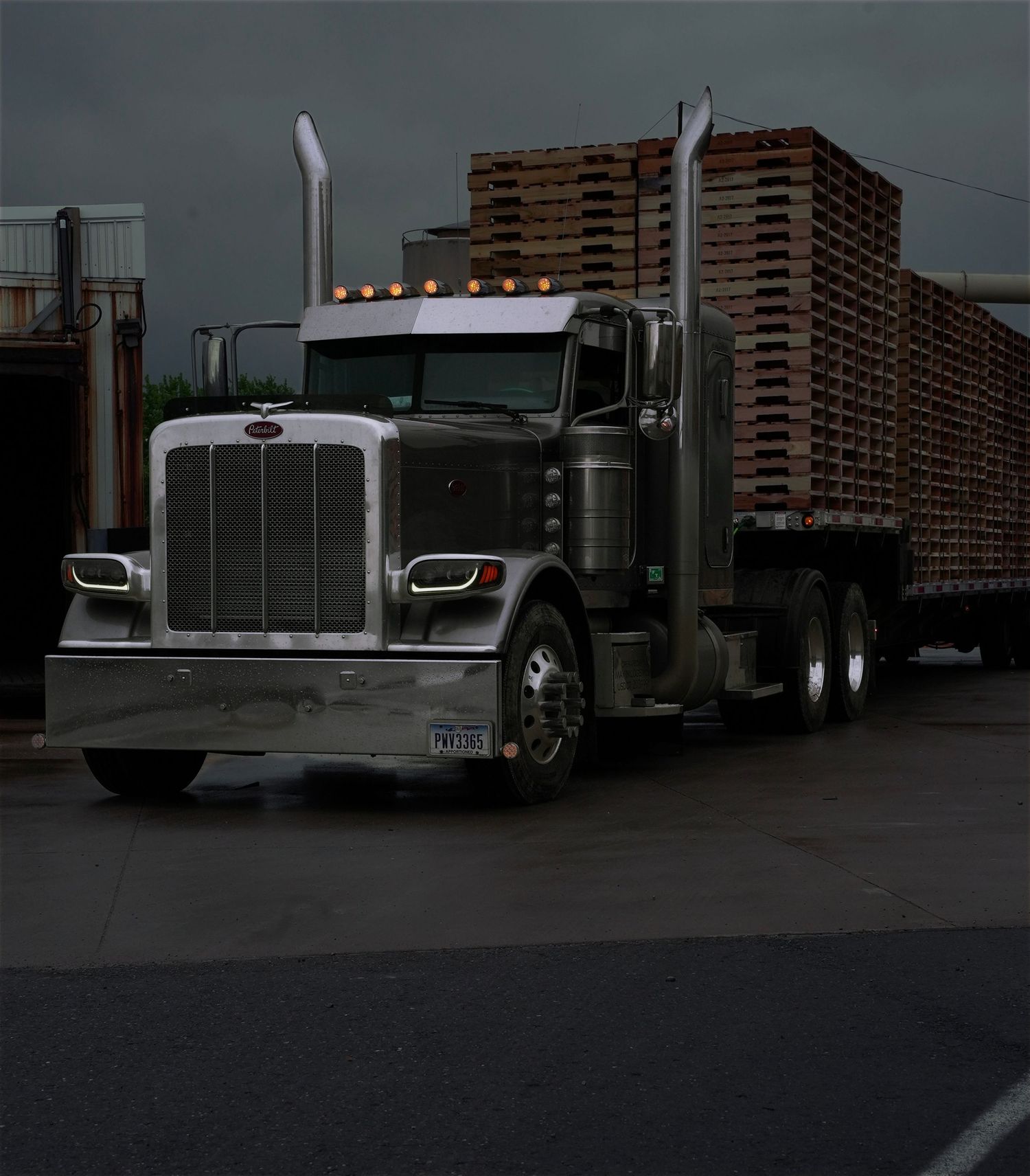 A grey Peterbilt semi truck with a step deck load of wood pallets