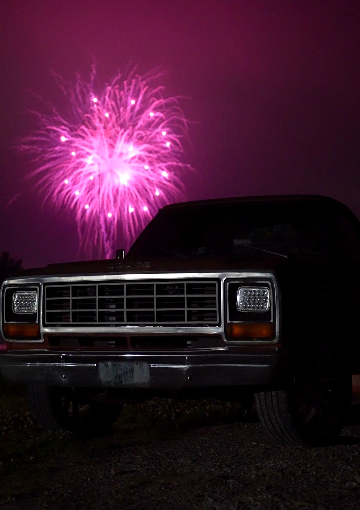 An old dodge truck in front of pink fireworks