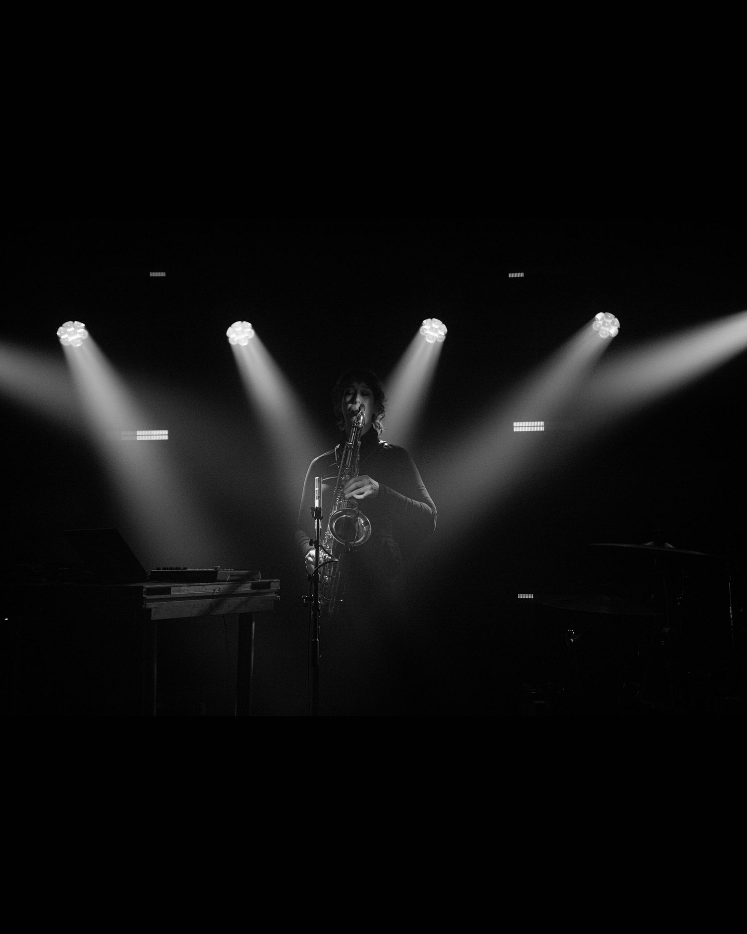 Black and white photo of a musician performing on a dark stage illuminated by dramatic spotlights from above.