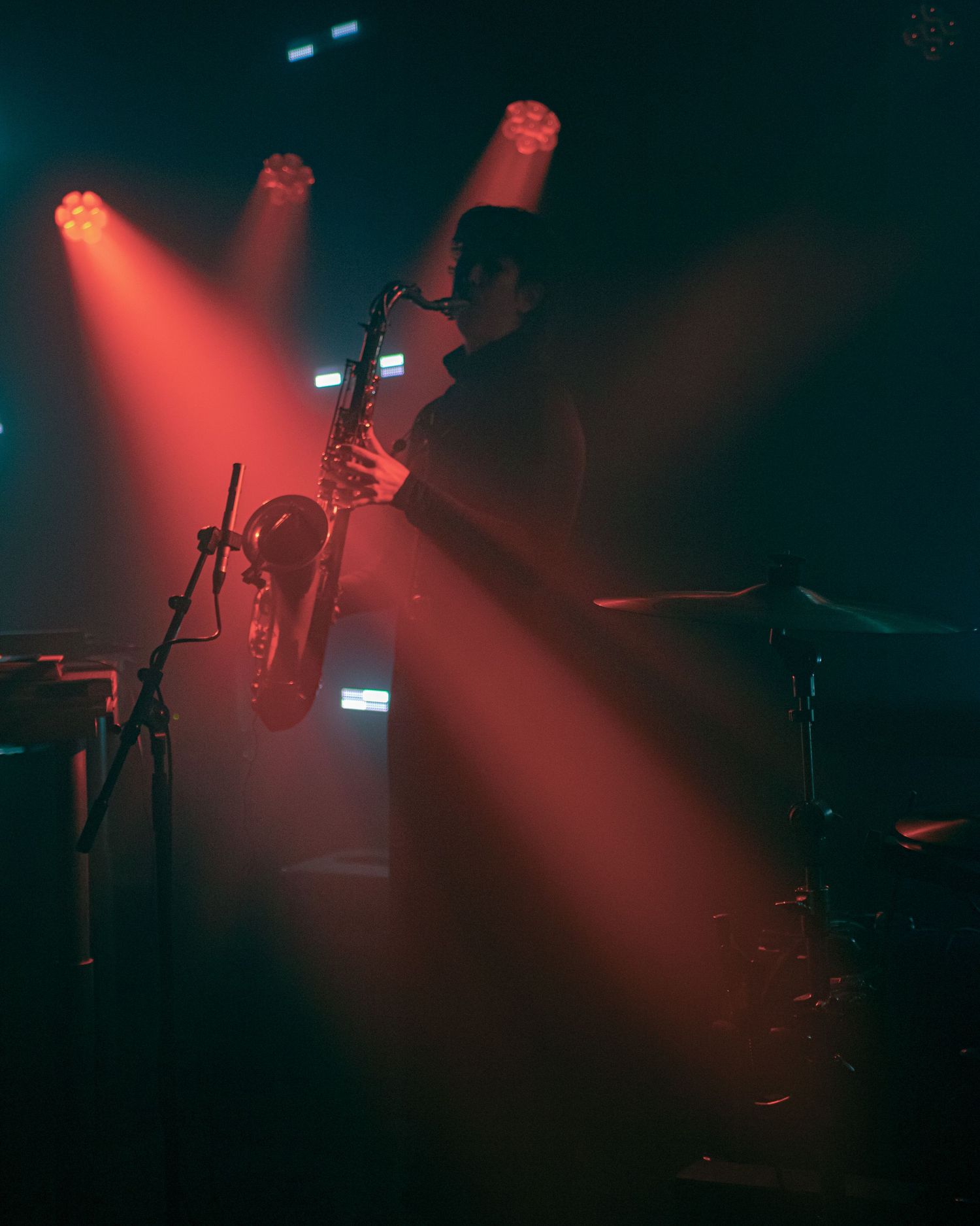 Silhouetted saxophonist performing on stage under dramatic red spotlights in a dark concert venue.