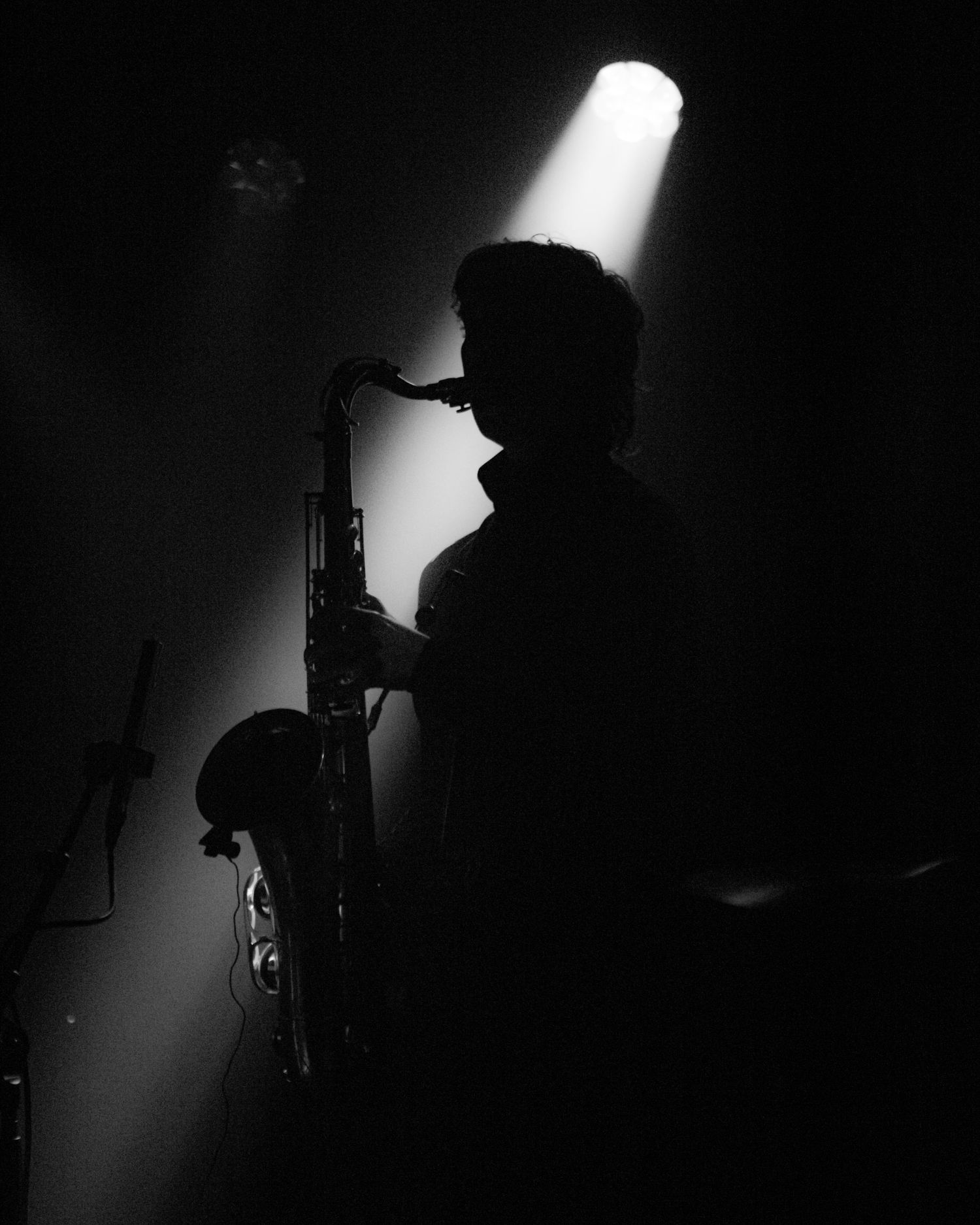 Silhouette of a saxophonist performing on stage under a single spotlight in dramatic black and white.