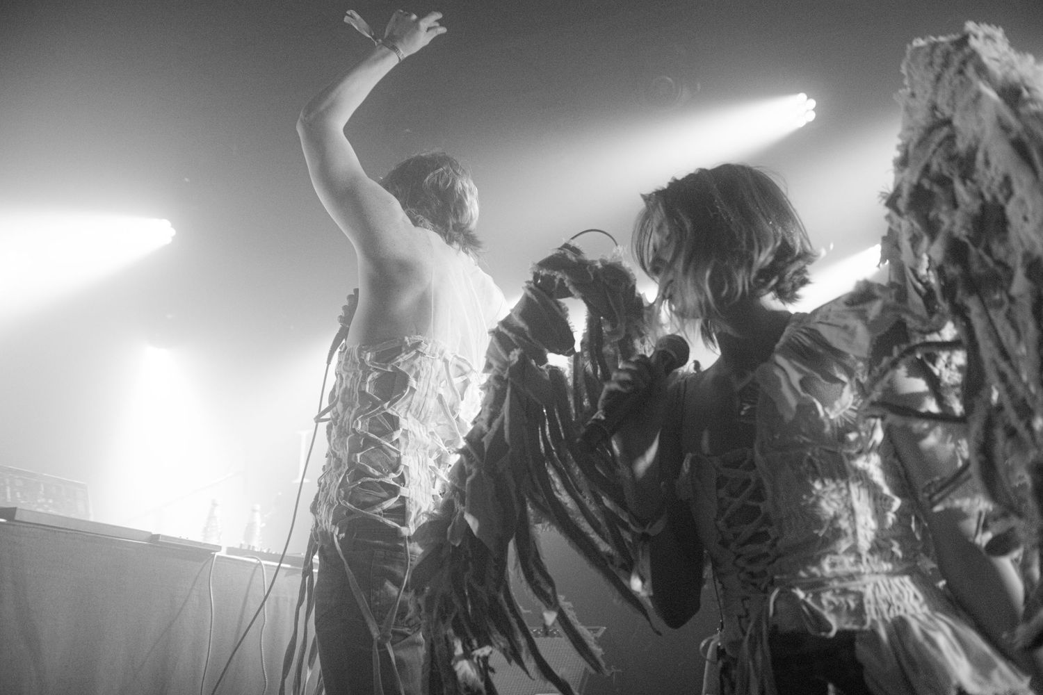 Two performers in elaborate costumes on stage under bright lights in a black and white concert photo.