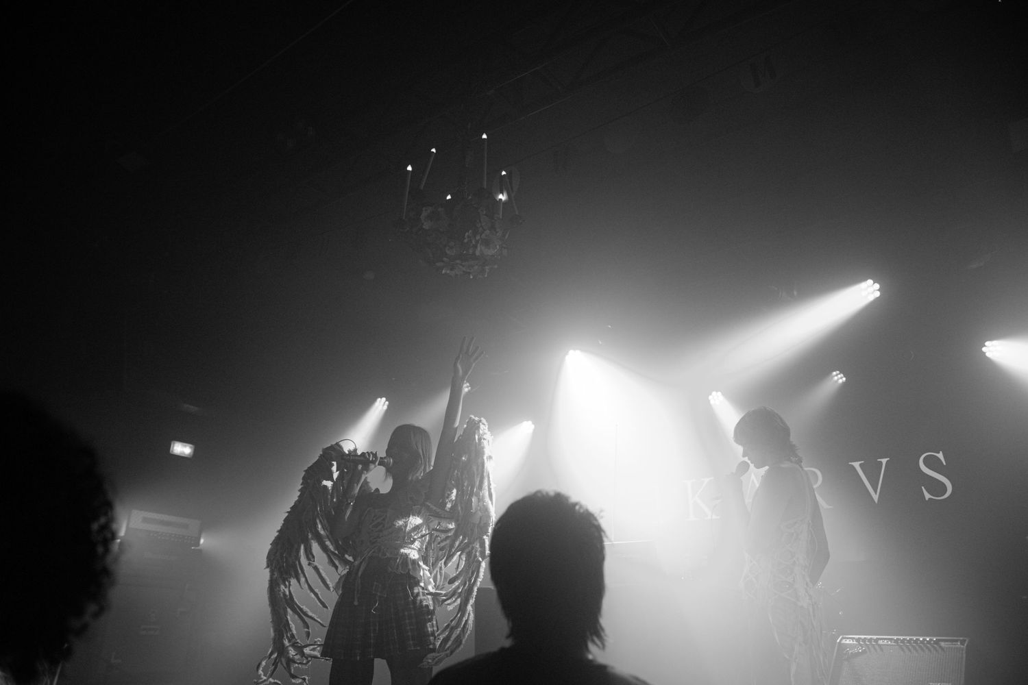 Black and white concert photo of band performing on stage with dramatic backlighting and spotlight effects.